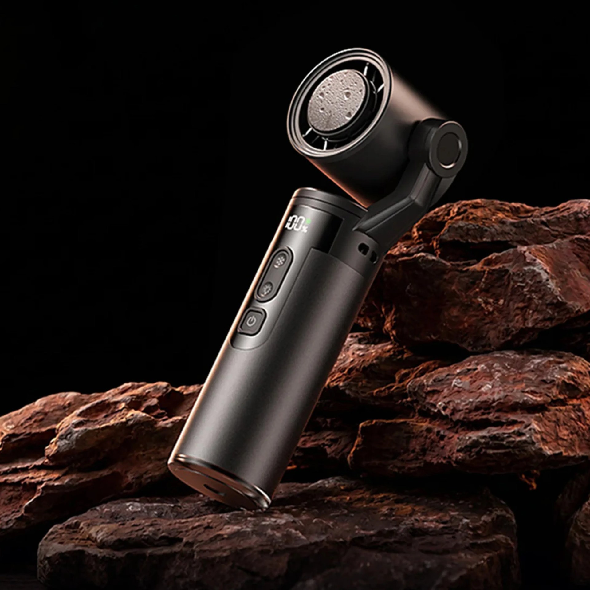 Black handheld electric shaver with digital display resting on brown textured rocks.