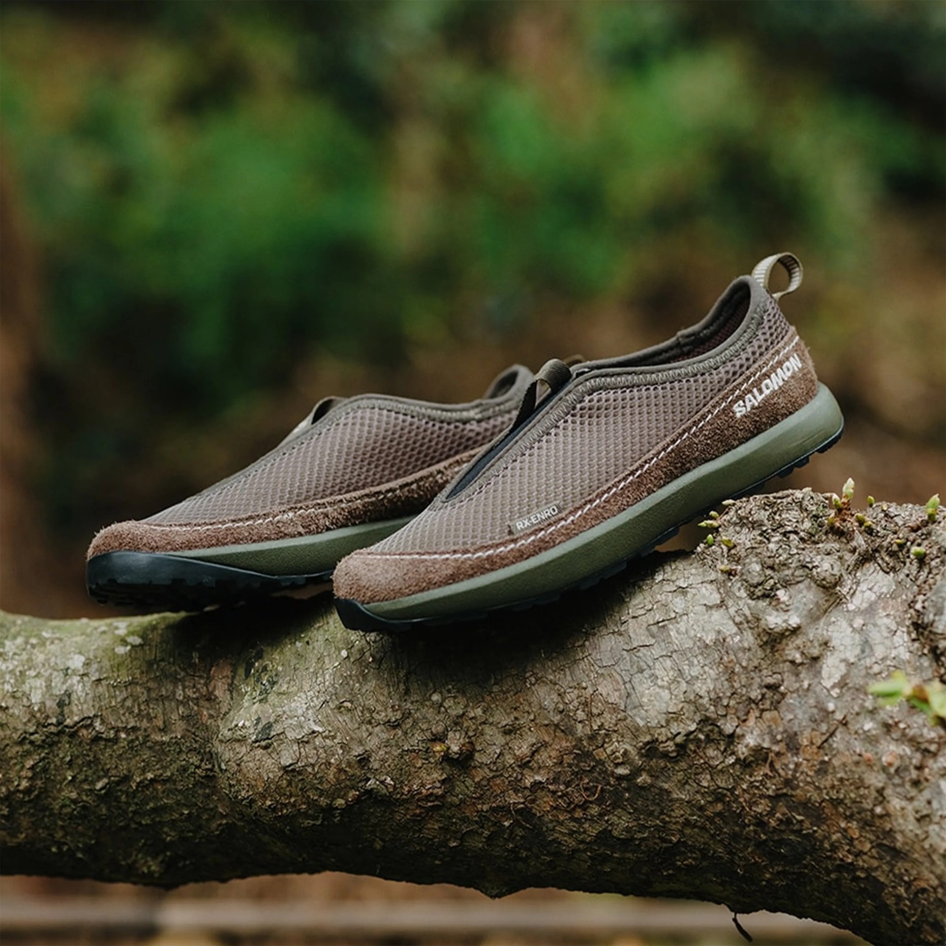 Brown and olive green Salomon slip-on shoes with mesh and suede uppers resting on a tree branch.