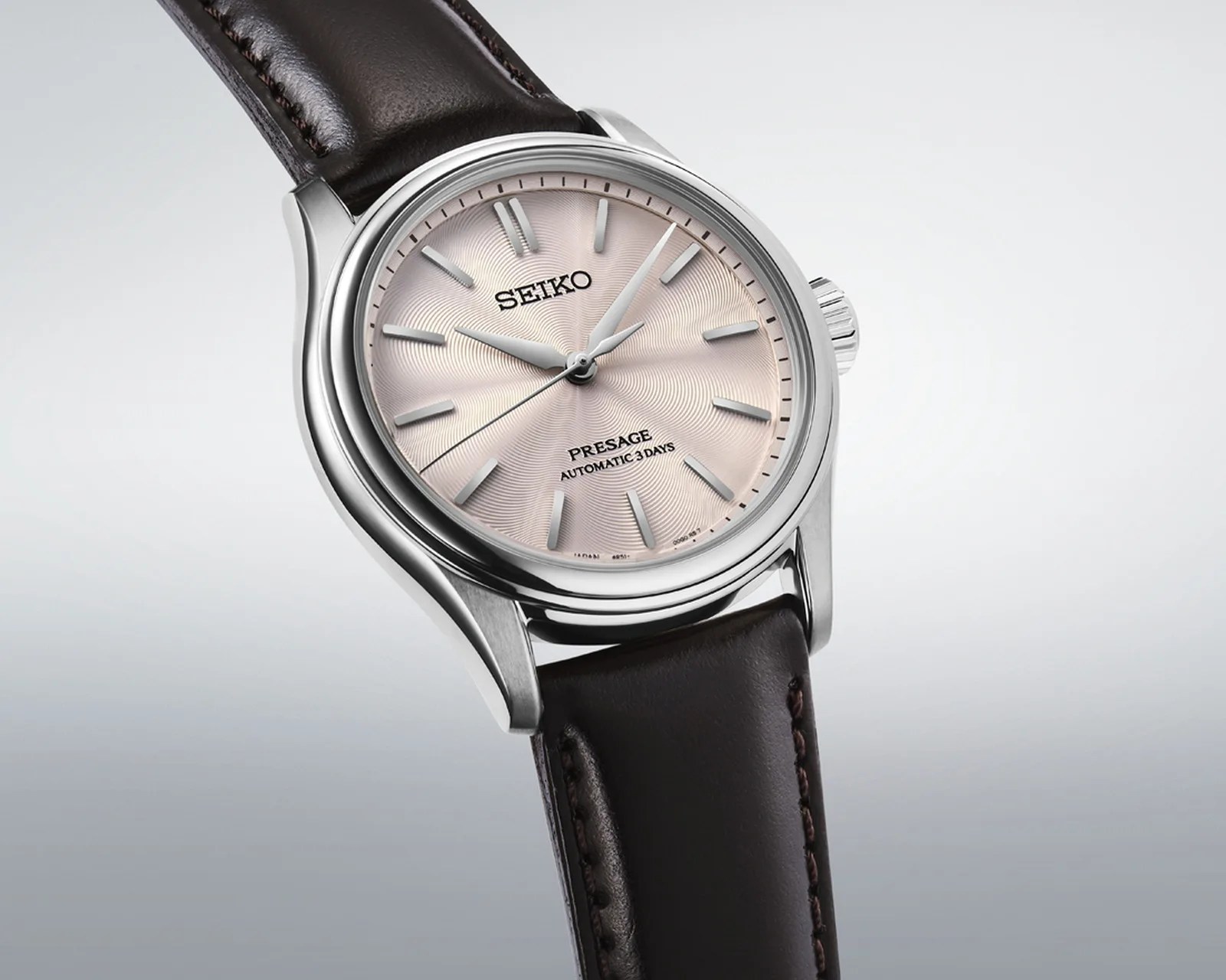 Silver Seiko Presage watch with a textured light pink dial and dark brown leather strap.