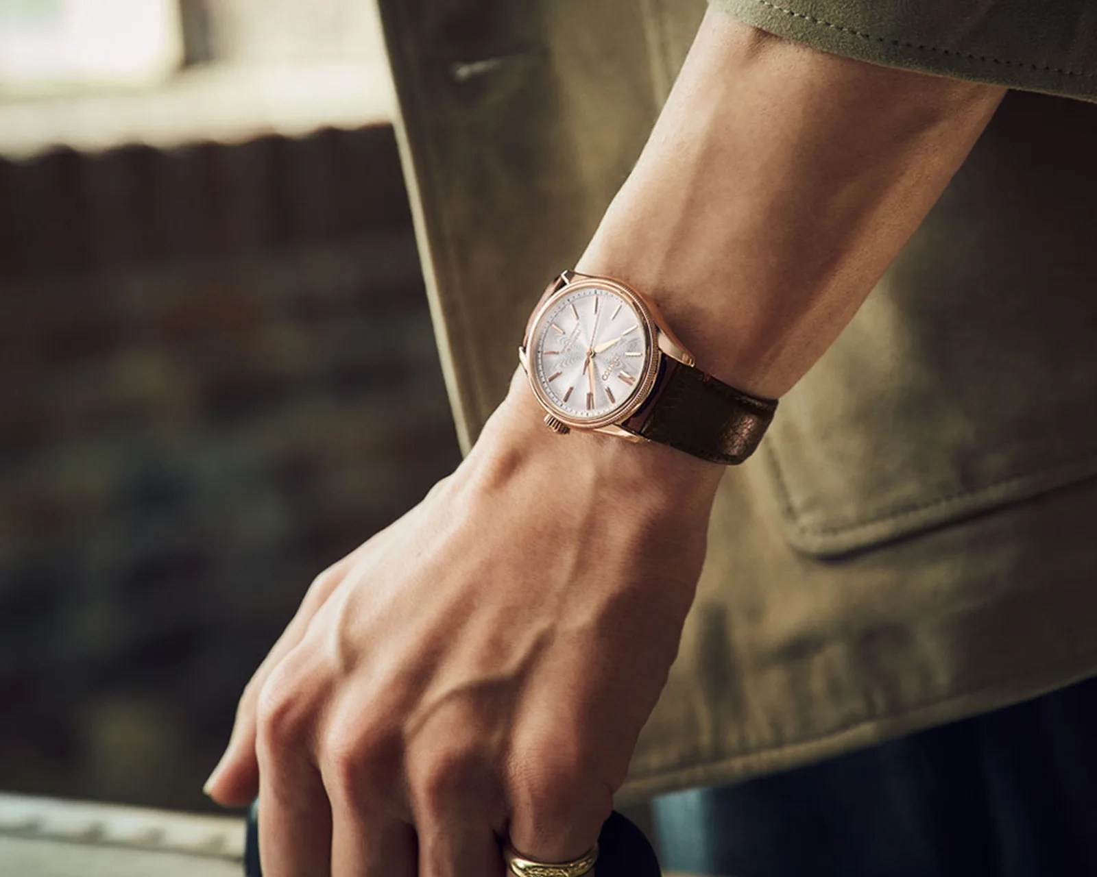 Wristwatch with a rose gold case, white dial, and black leather strap worn on a wrist.