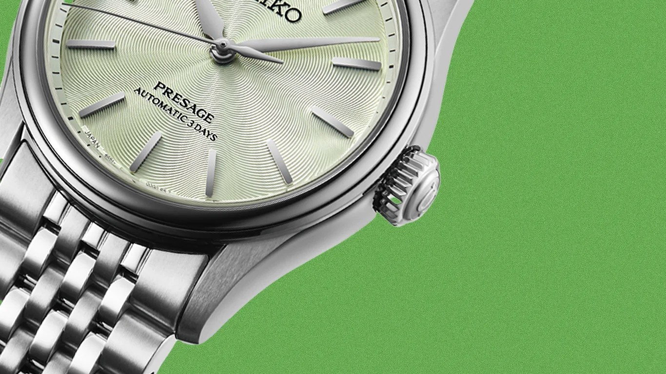 Close-up of a silver Seiko Presage watch with a textured light green dial and metal bracelet on a green background.