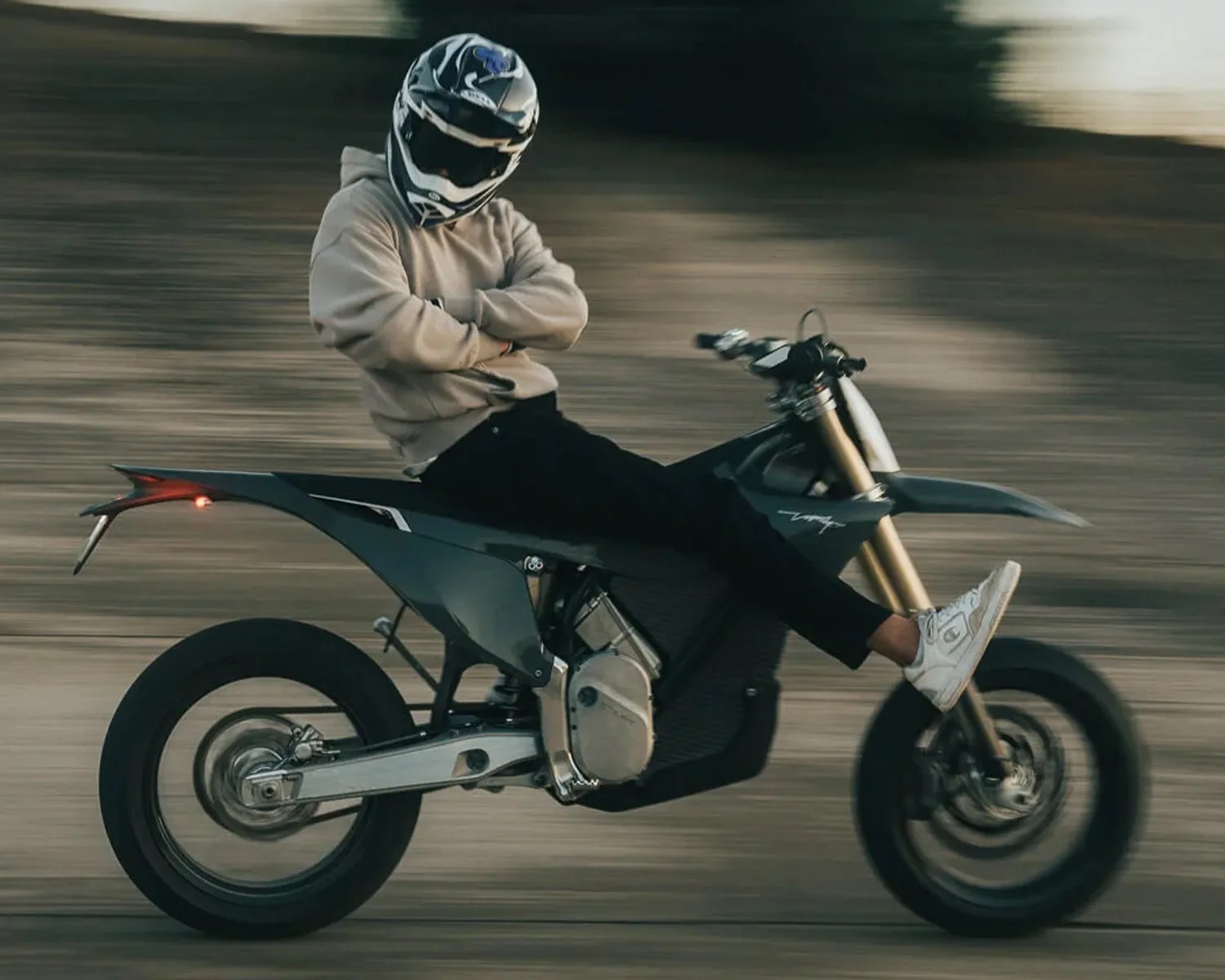Person wearing a black and white helmet and beige hoodie riding a black electric motorcycle with gold front forks.