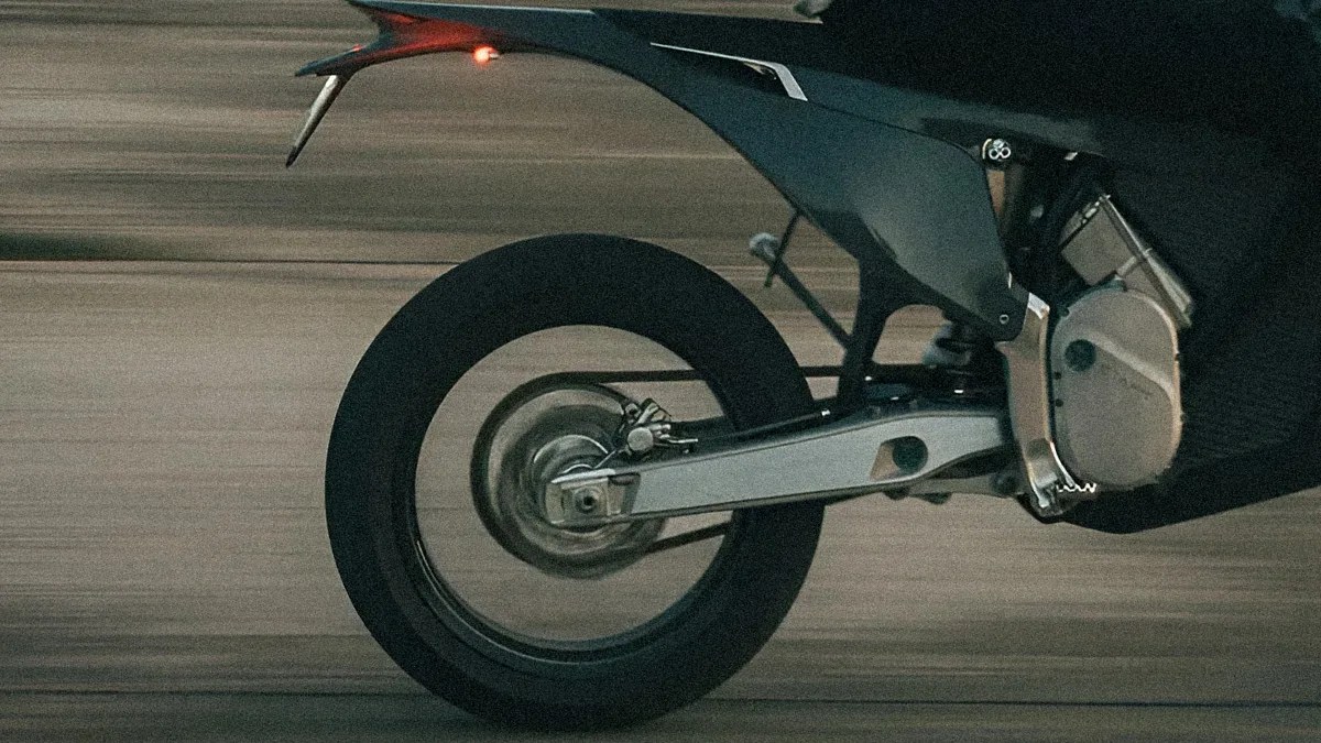 Rear wheel and suspension of a black motorcycle in motion on a blurred road background.