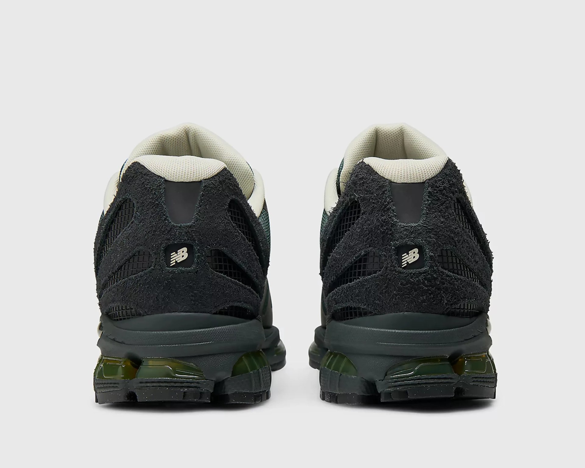 Pair of black New Balance sneakers with textured suede and mesh uppers, beige inner lining, and green-tinted soles viewed from the back.