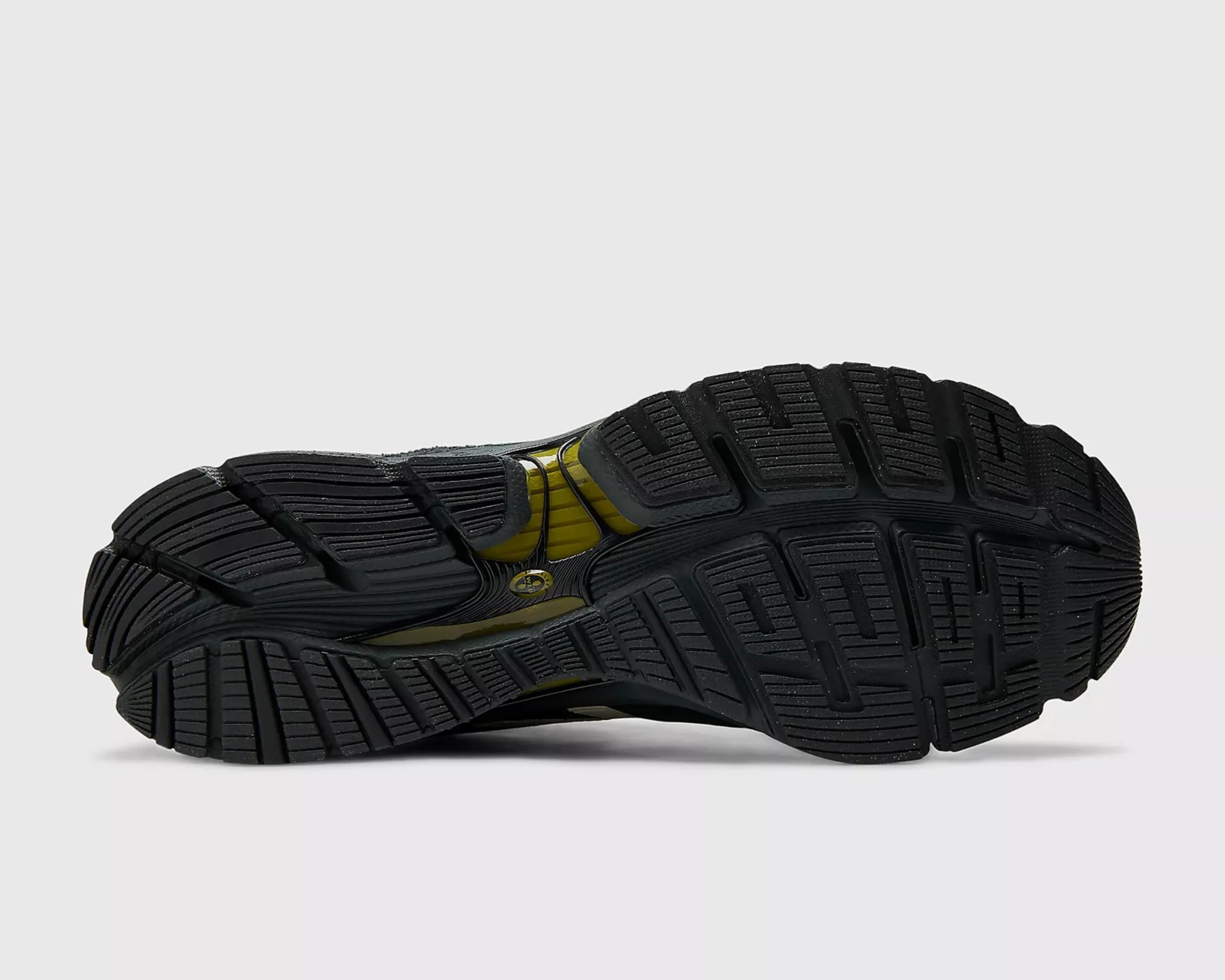 Black rubber sole of a shoe with deep grooves and yellow cushioning visible through the midsole.
