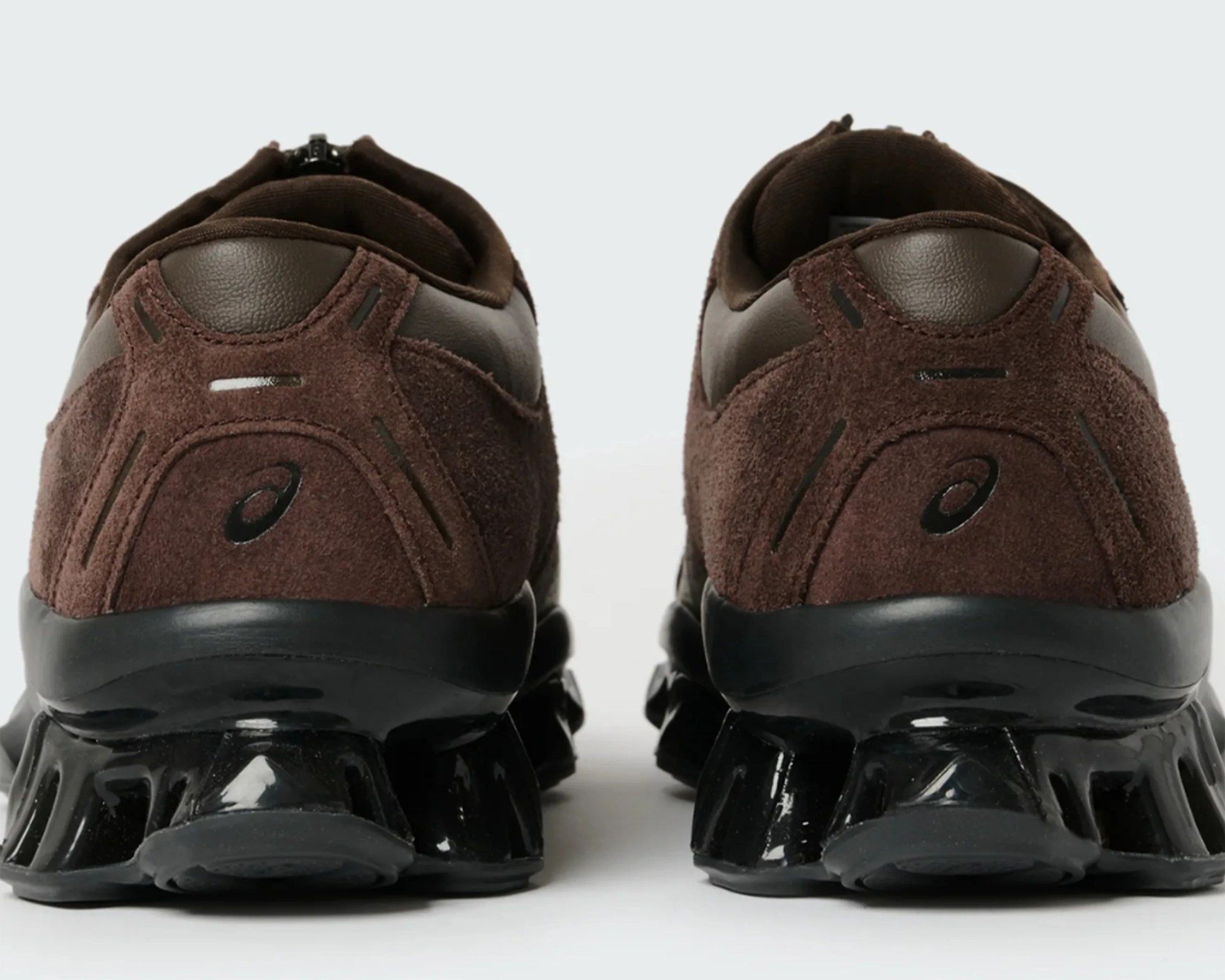 Pair of brown suede and leather sneakers with black glossy segmented soles, viewed from the back.