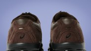 Pair of brown suede and leather sneakers with black soles viewed from the back against a blue background.