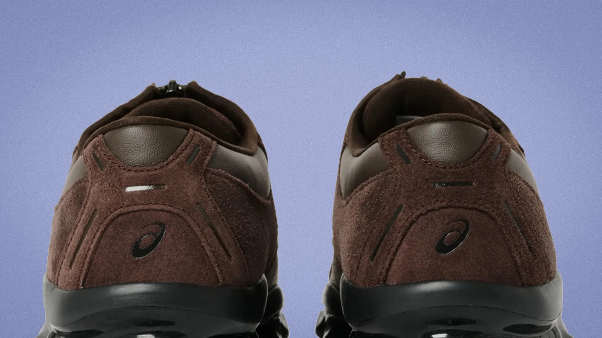 Pair of brown suede and leather sneakers with black soles viewed from the back against a blue background.