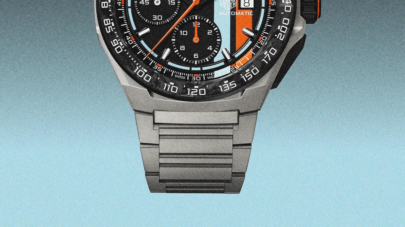 Close-up of a TAG Heuer automatic chronograph watch with a black, orange, and light blue dial and a silver metal bracelet.