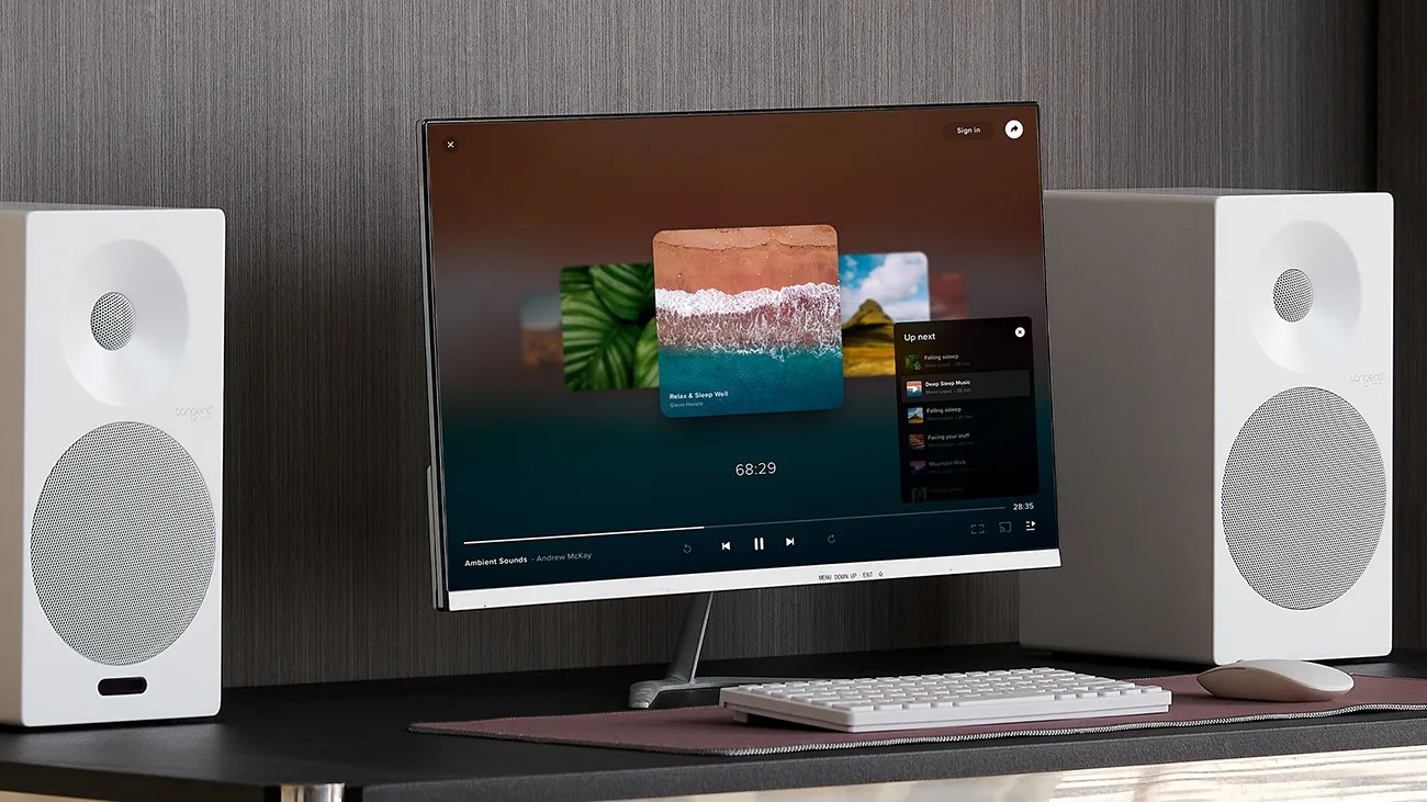Curved widescreen monitor displaying music app, flanked by white Tangent speakers, with white keyboard and mouse on desk.