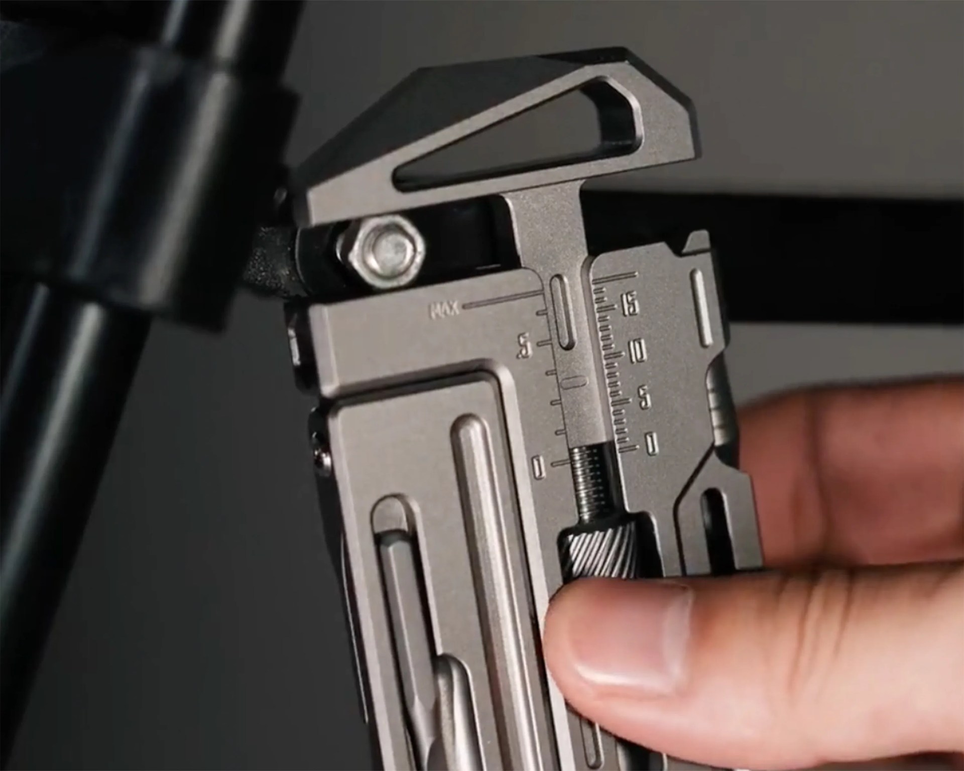 Close-up of a hand adjusting a silver multi-tool with measurement markings and a bolt.