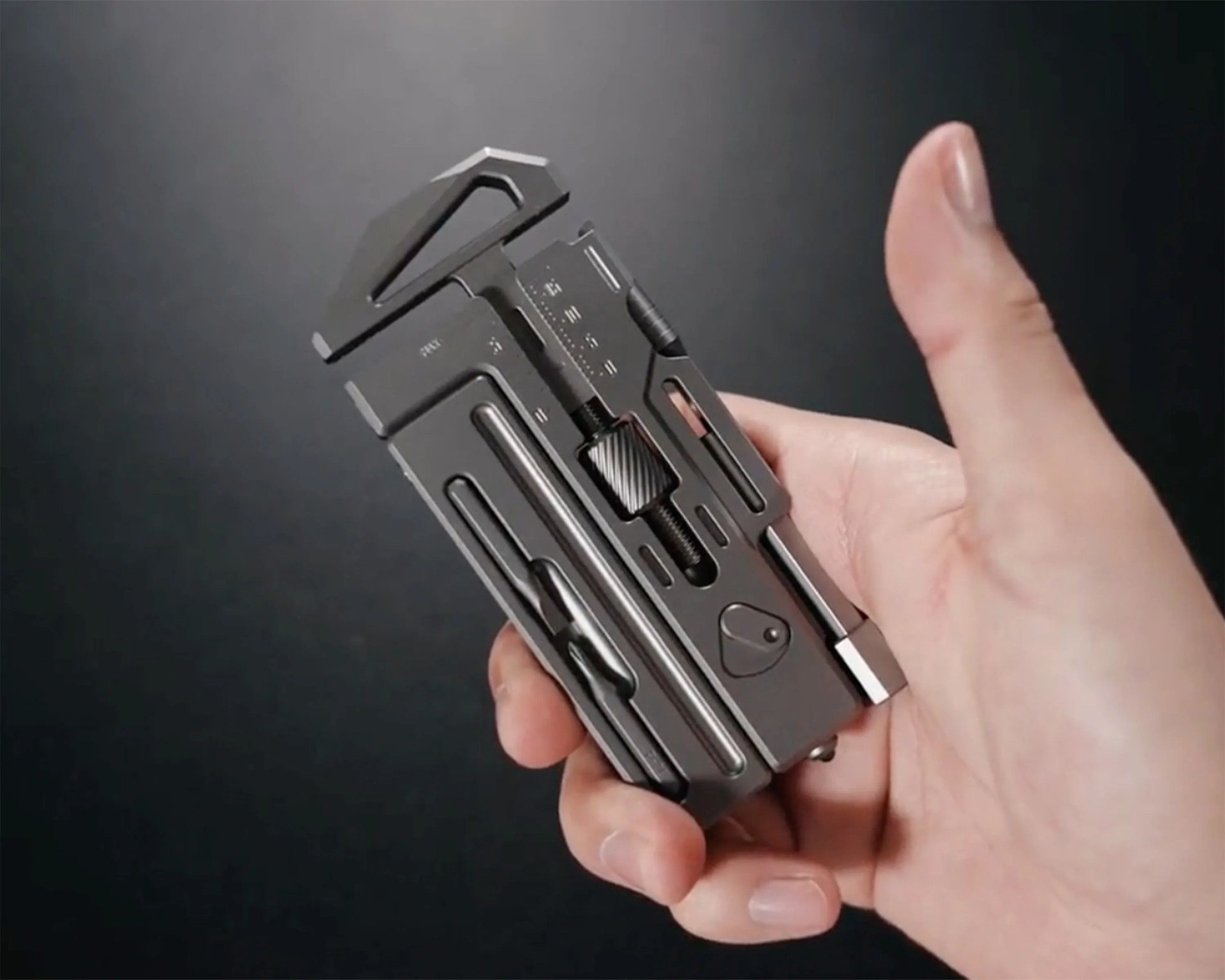 Compact black multi-tool with various metal tools held in a hand against a dark background.