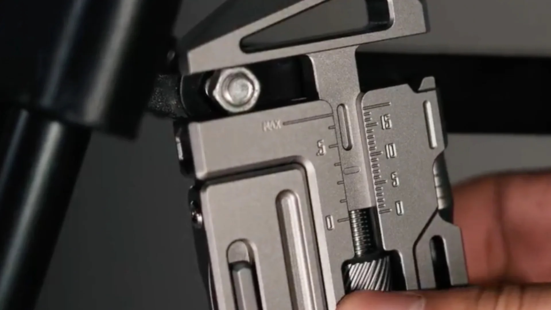 Close-up of a metallic caliper measuring tool with engraved scale markings and a black adjustment knob held by a hand.