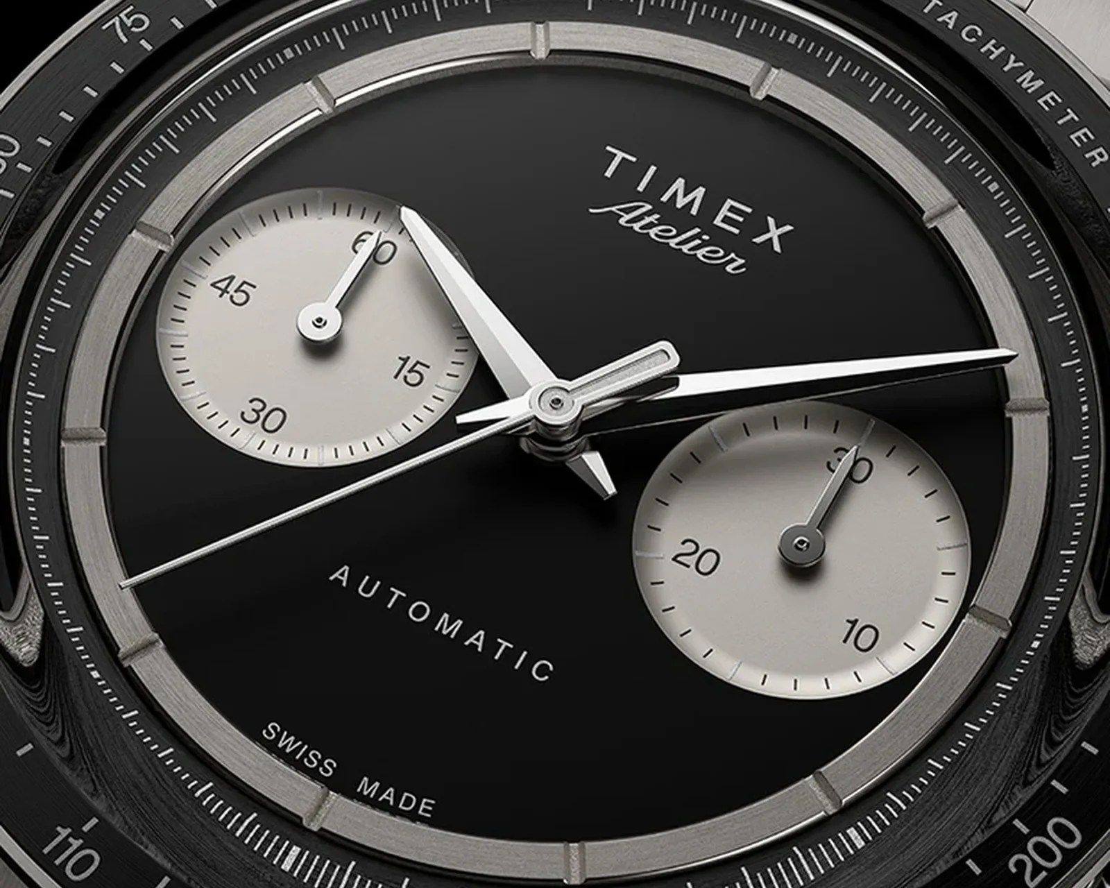 Close-up of a Timex Atelier automatic watch face with black dial, silver subdials, and tachymeter bezel.
