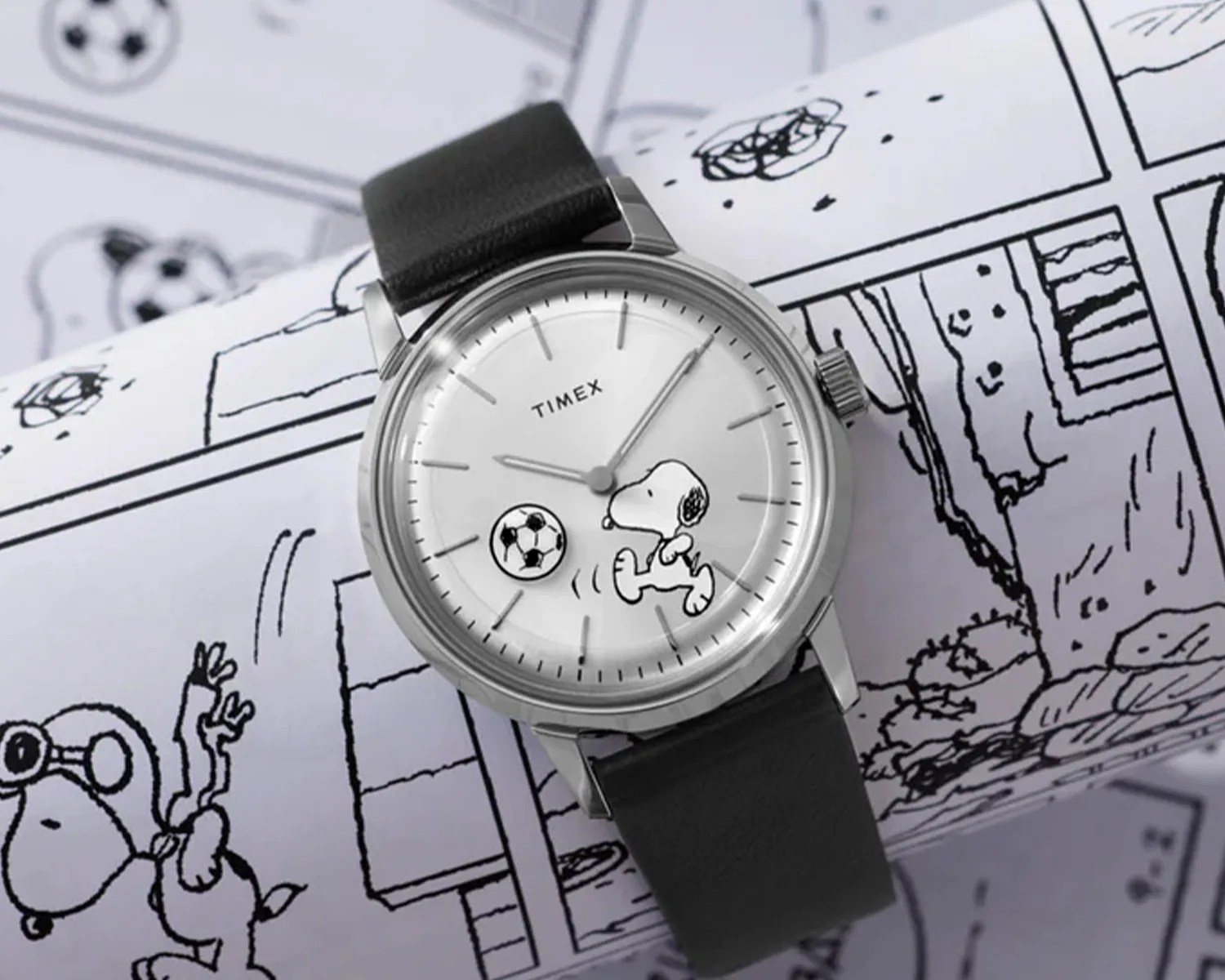 Silver Timex wristwatch with black leather strap and Snoopy playing soccer on the white dial.