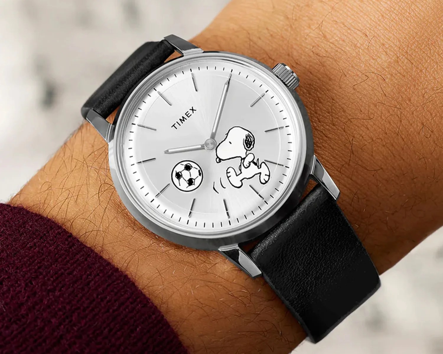 Silver Timex wristwatch with black leather strap and Snoopy playing soccer on the white dial.