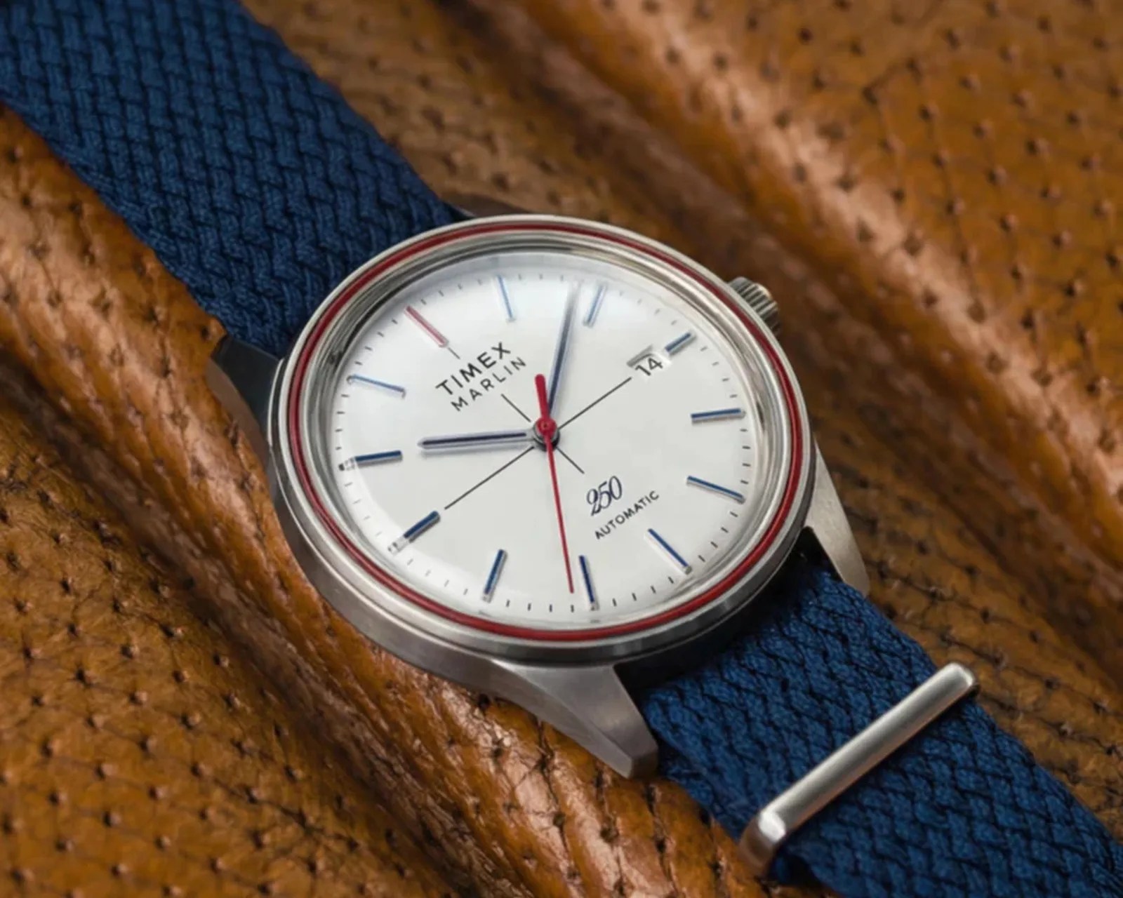 Timex Marlin automatic watch with white dial, blue hour markers, red second hand, and blue woven strap on brown leather.