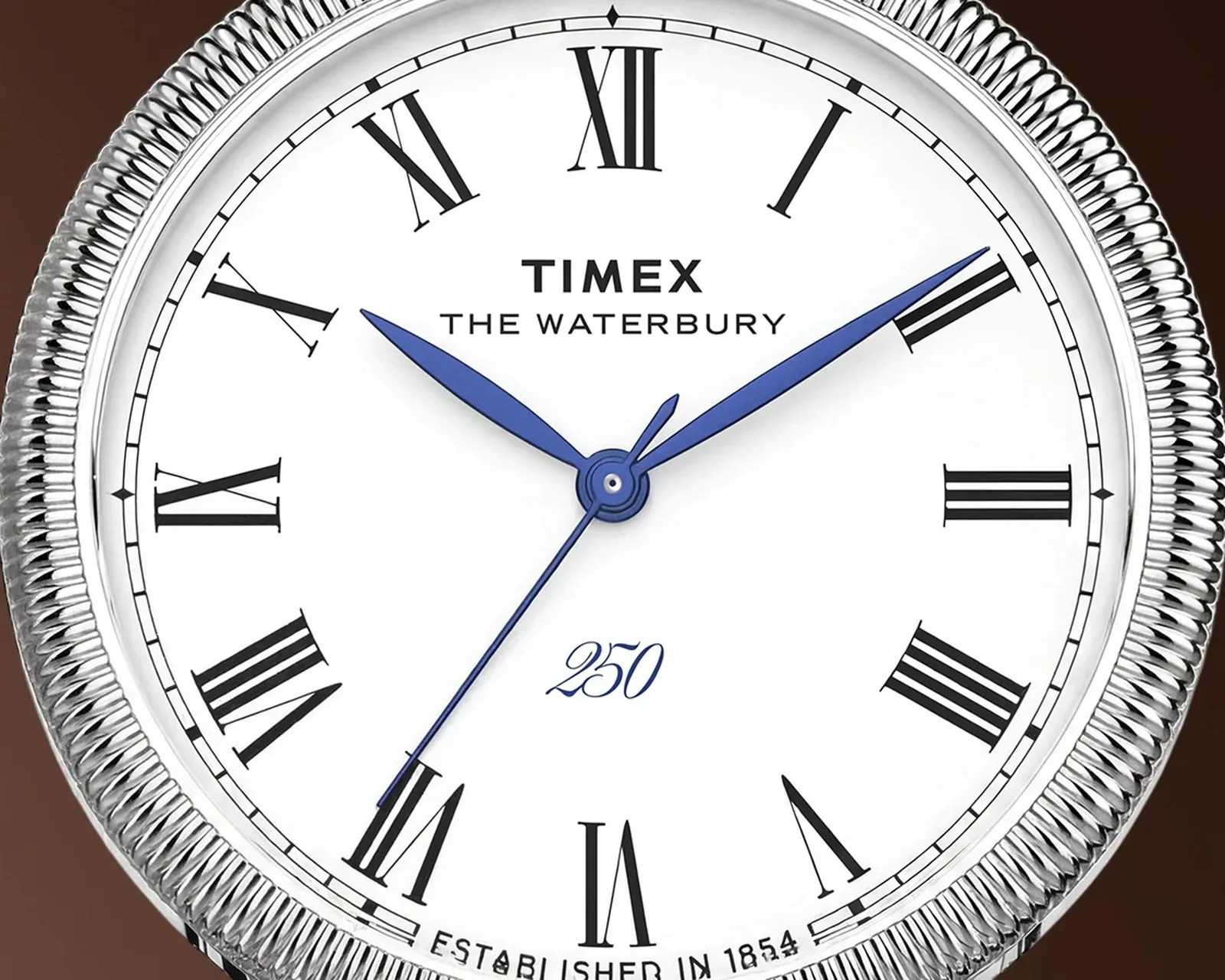 Close-up of a Timex The Waterbury watch face with blue hands, Roman numerals, and a silver ridged bezel.