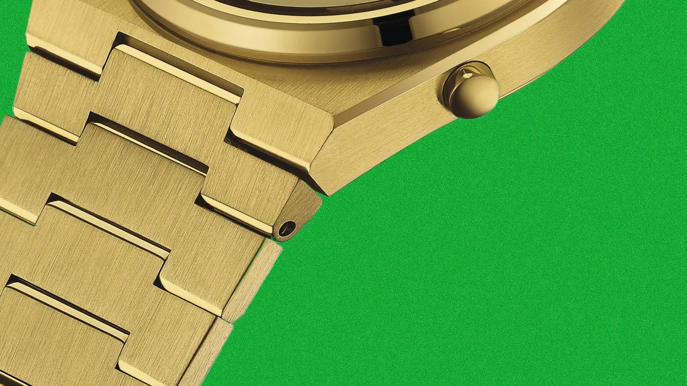 Close-up of a gold-toned metal watch bracelet and case with a brushed finish against a green background.