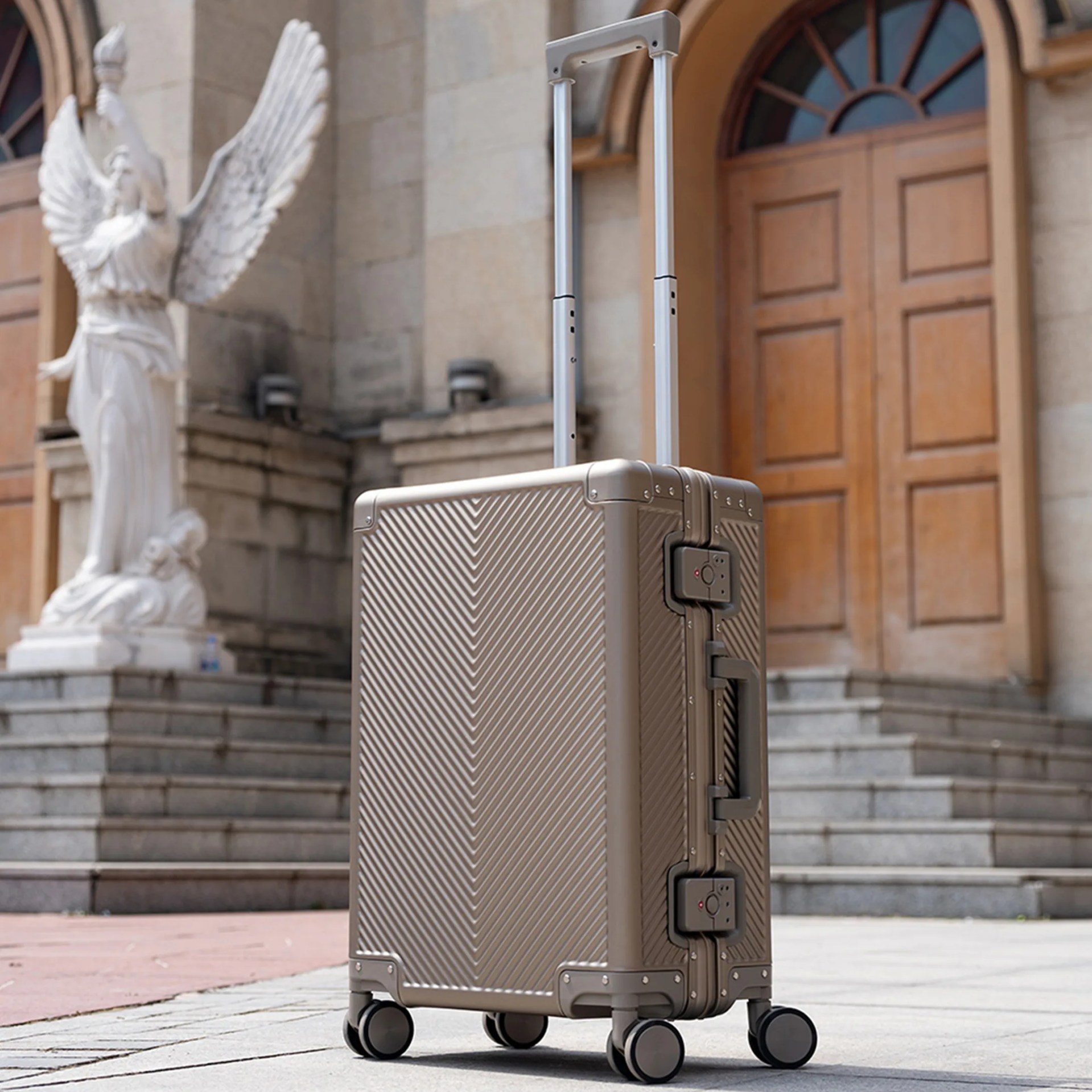 Metallic silver hard-shell suitcase with four wheels and extended telescopic handle on pavement.