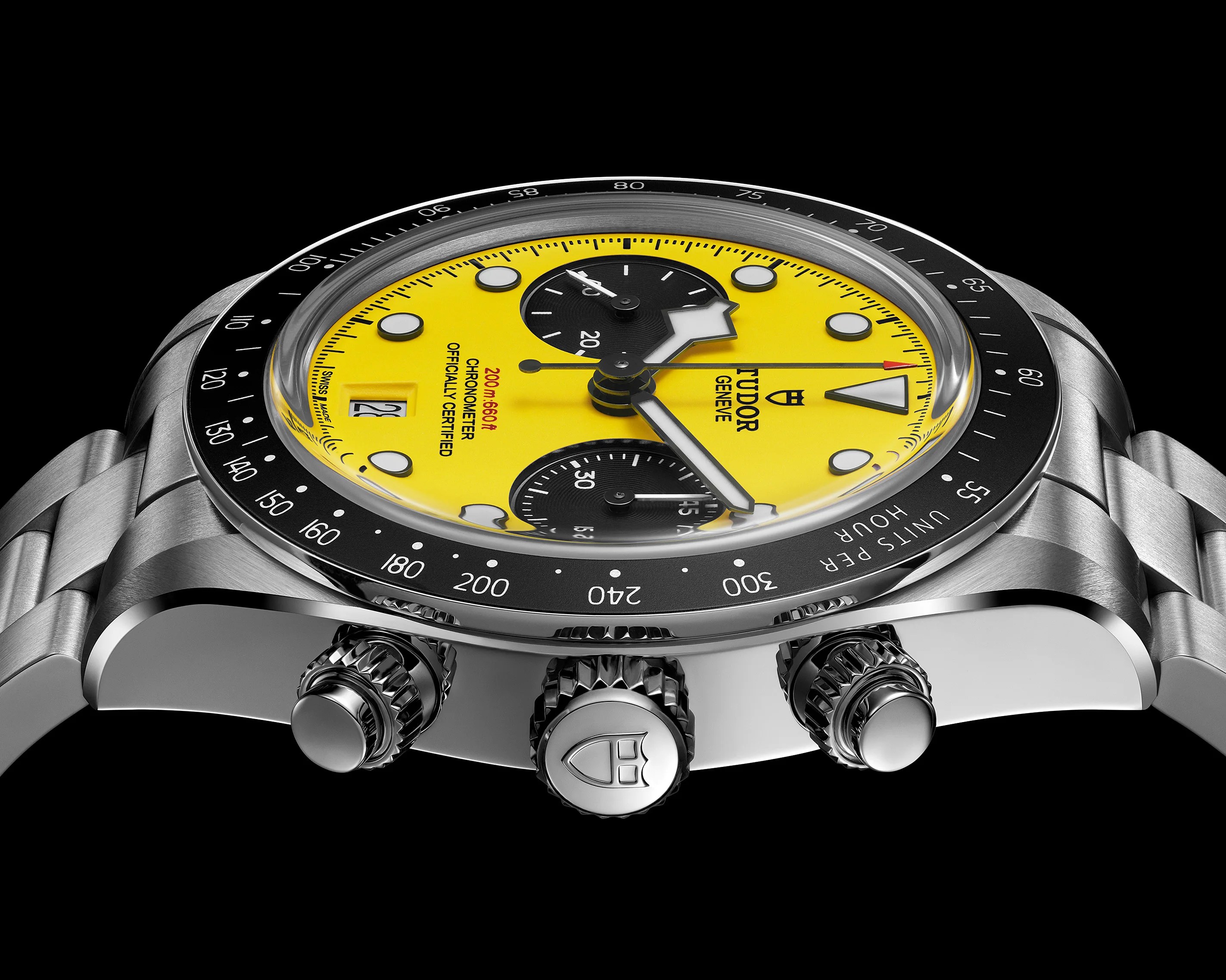 Close-up of a Tudor chronograph watch with a yellow dial, black subdials, stainless steel case, and black bezel.