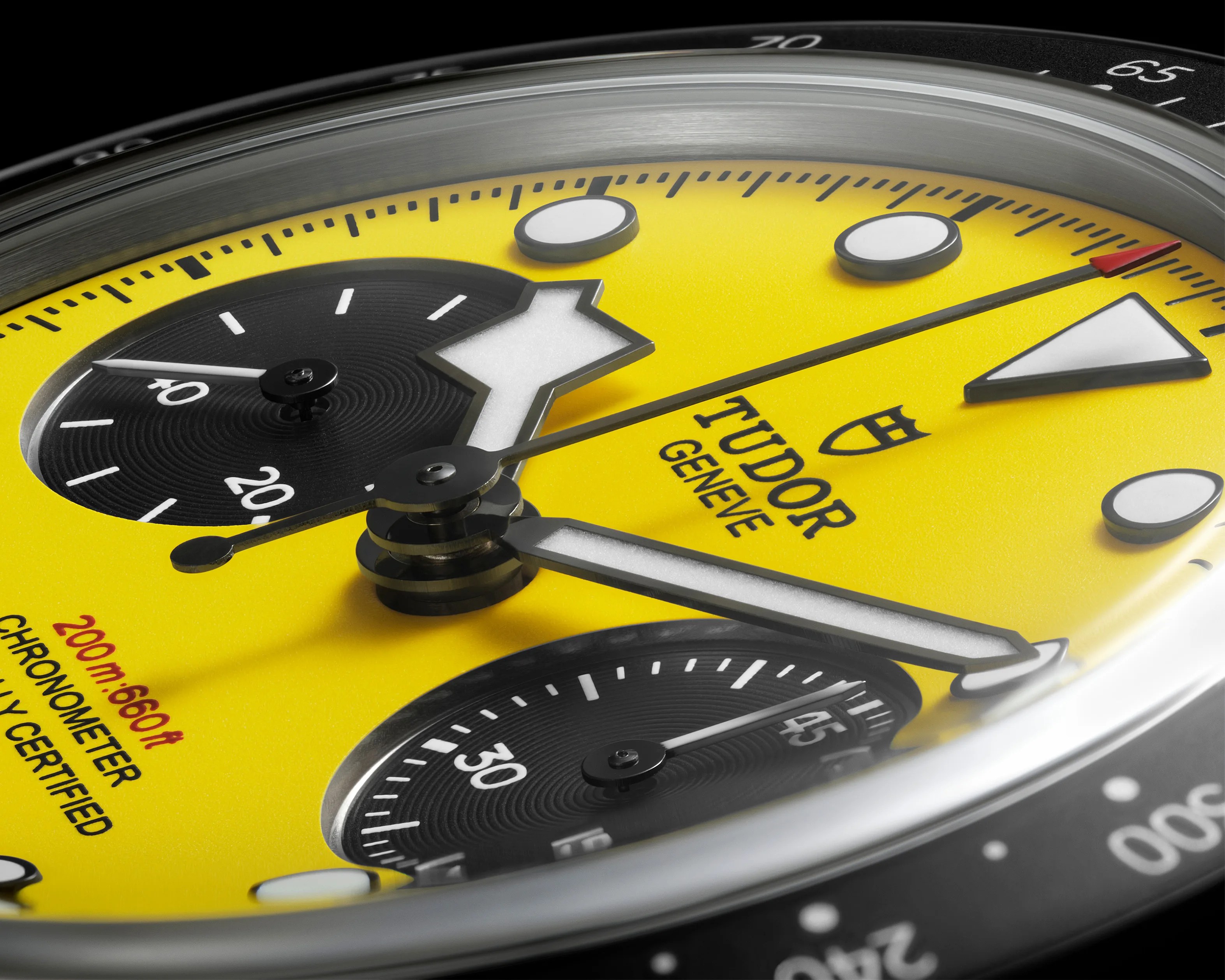 Close-up of a Tudor Gen&egrave;ve yellow watch dial with black subdials, white markers, and a red-tipped second hand.