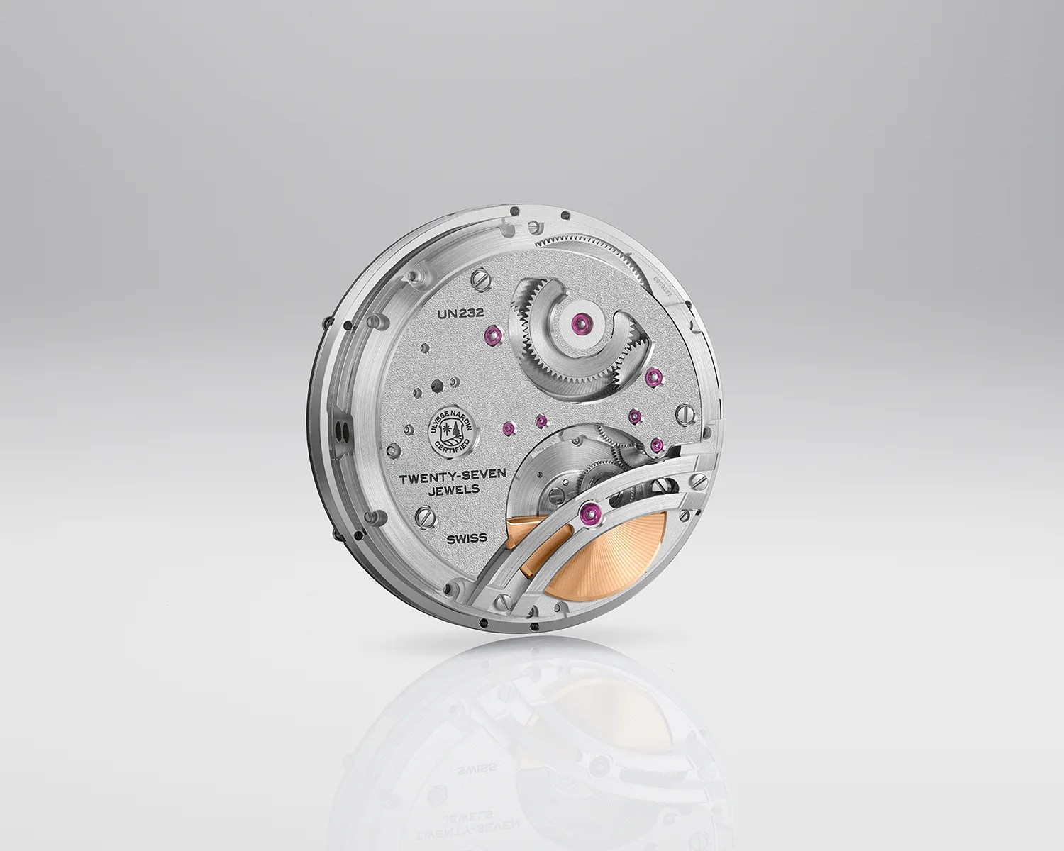 Silver watch movement with visible gears, purple jewels, and a gold-toned rotor on a reflective surface.