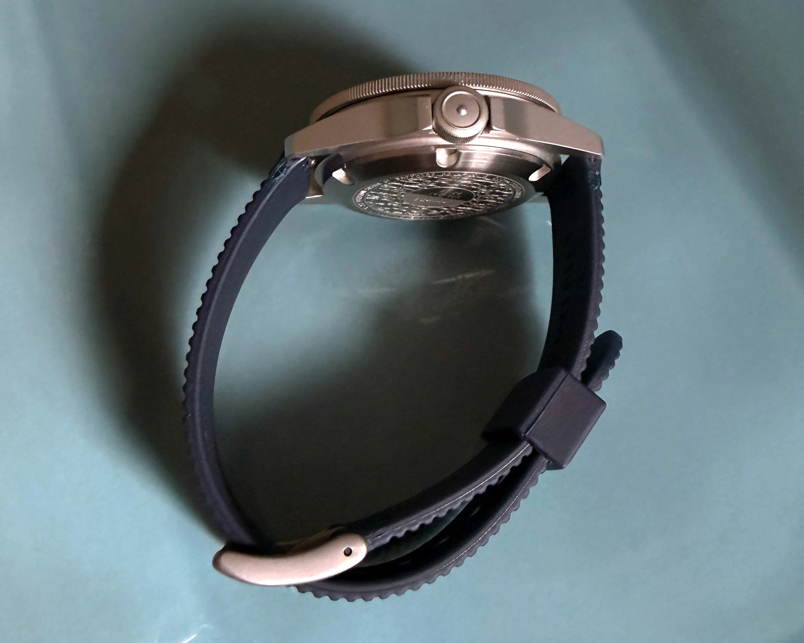 Silver wristwatch with black rubber strap viewed from the side on a blue surface.