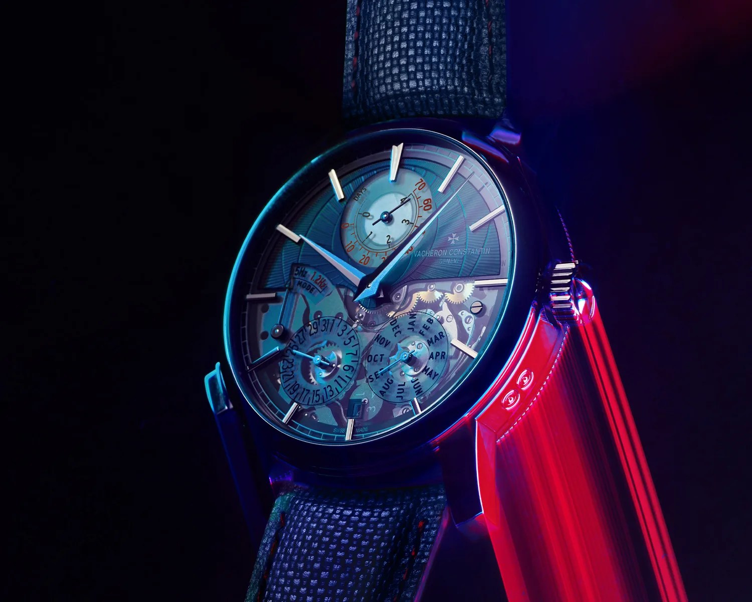 Luxury wristwatch with a transparent dial showing gears and calendar functions, illuminated by blue and red lighting.