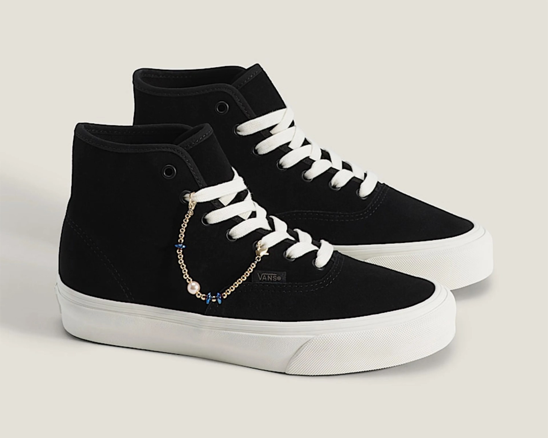 Black Vans high-top sneakers with white laces, white soles, and a gold chain accessory with blue beads and a pearl.