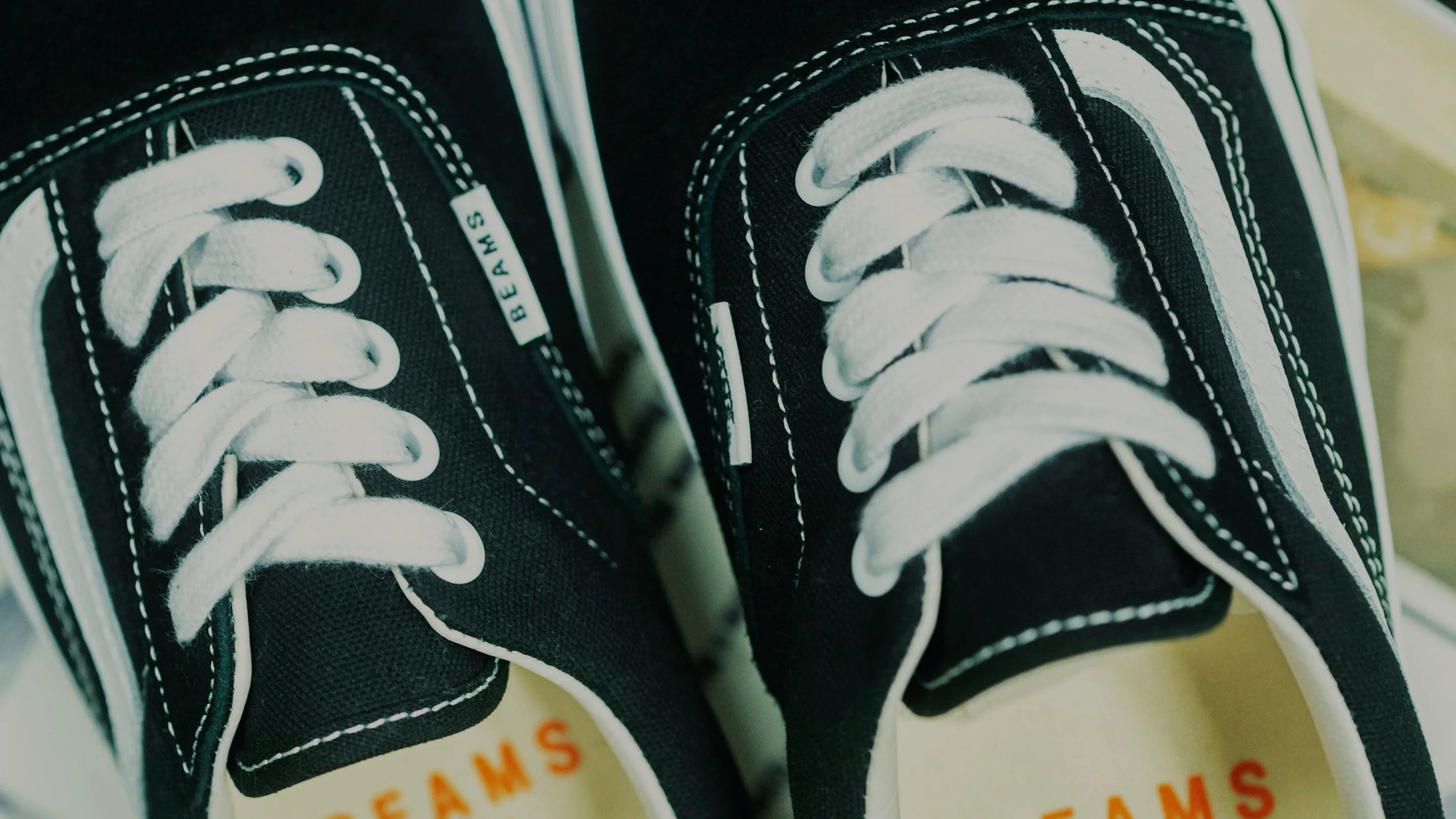 Close-up of black canvas sneakers with white laces and white side stripes, labeled "BEAMS" on the tongue tag.
