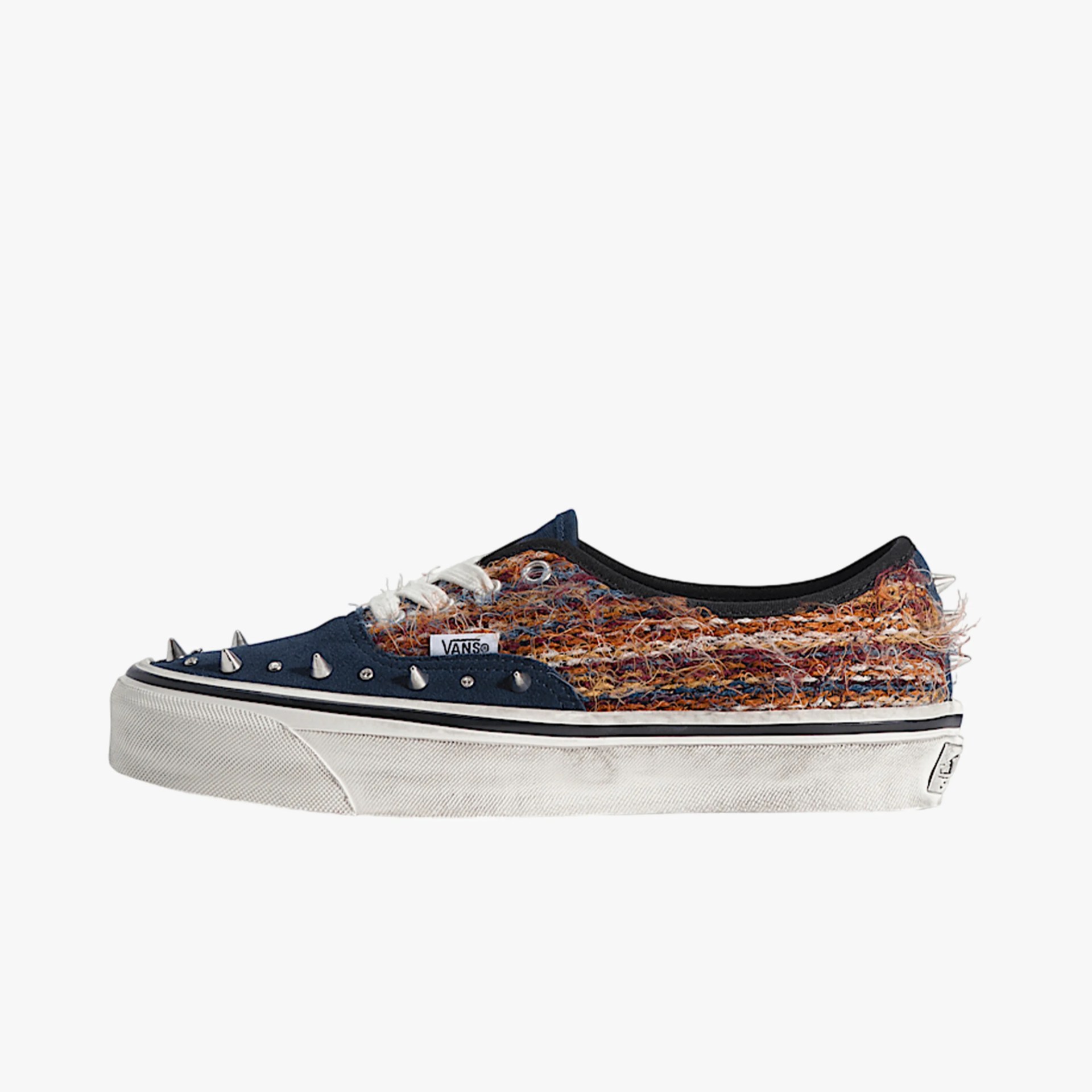 Navy blue Vans sneaker with multicolored fuzzy fabric, white laces, metal spikes, and white rubber sole.