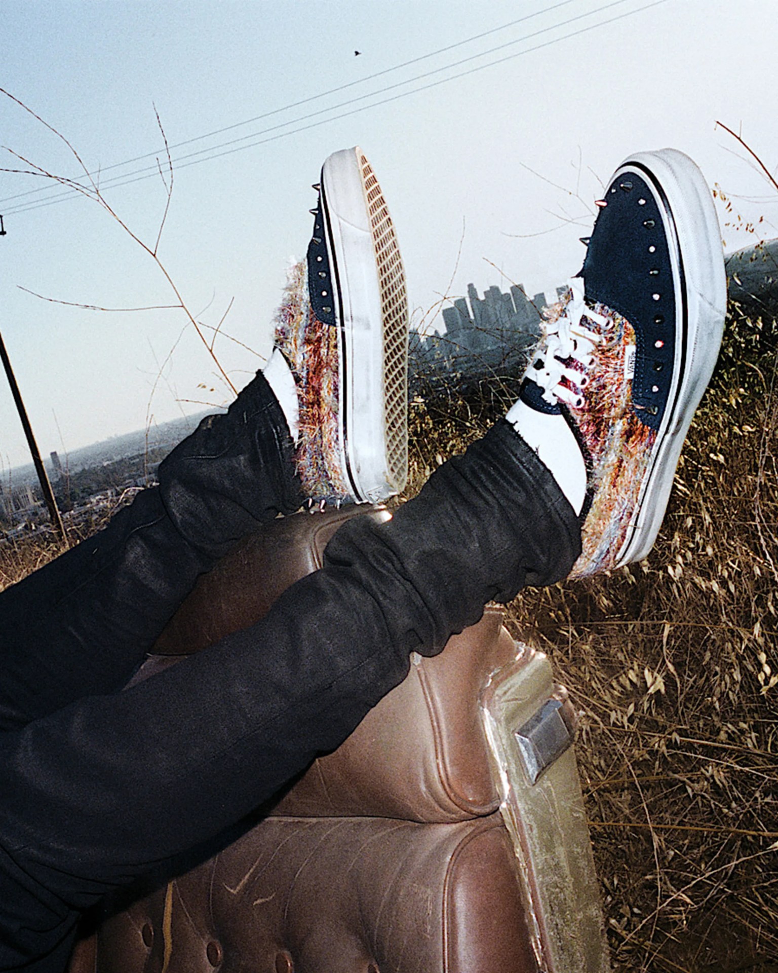 Navy and multicolor Vans sneakers with spikes worn with black pants and white socks, feet raised outdoors.