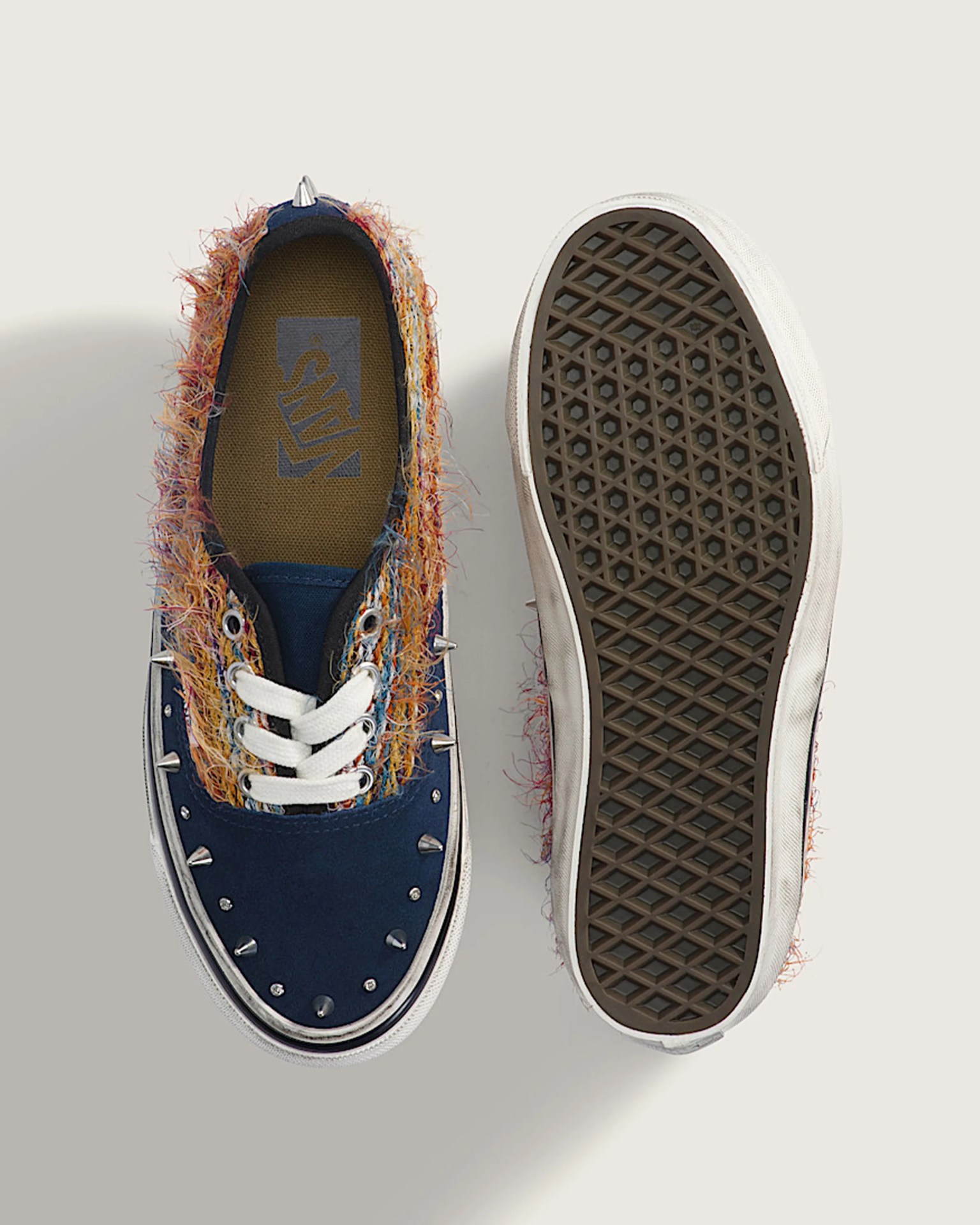 Pair of navy blue Vans sneakers with white laces, multicolored fuzzy trim, and silver spikes on a light background.