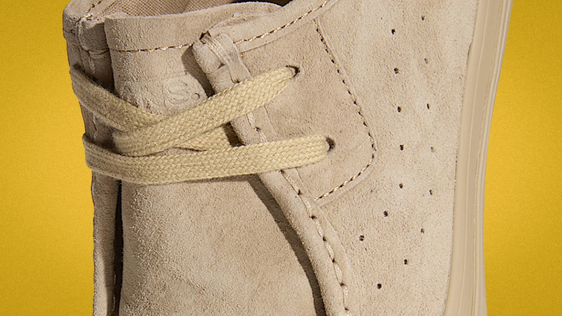 Close-up of beige suede shoe with beige laces and perforated side panel against a yellow background.