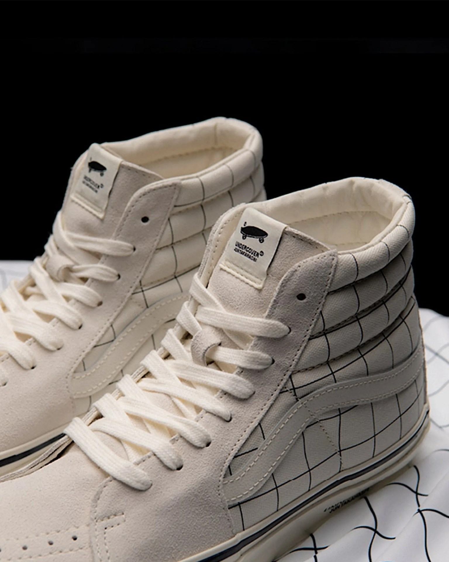 Pair of off-white high-top sneakers with black grid pattern and skateboard logo on tongue.