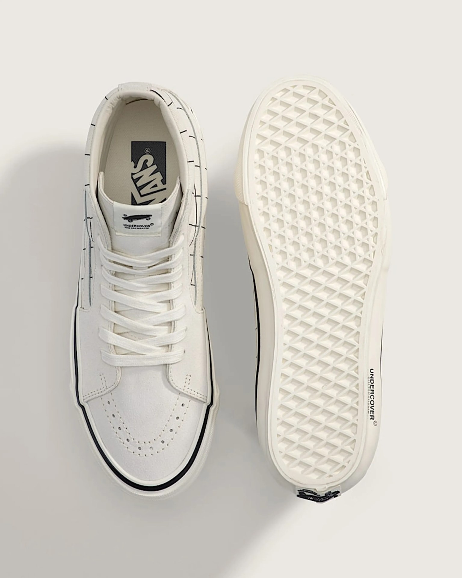 White Vans sneakers with black grid pattern and "UNDERCOVER" branding on sole and tongue label.