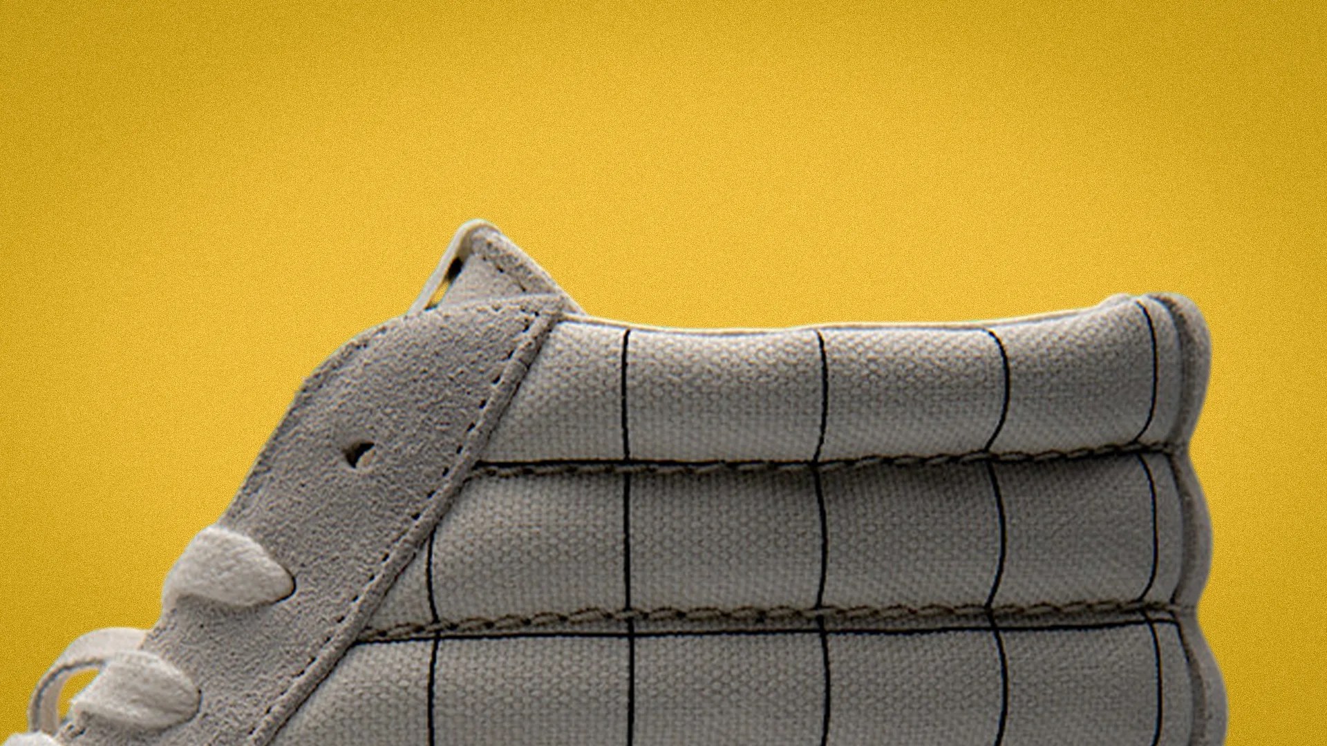 Close-up of a gray sneaker with grid pattern stitching and suede details against a yellow background.