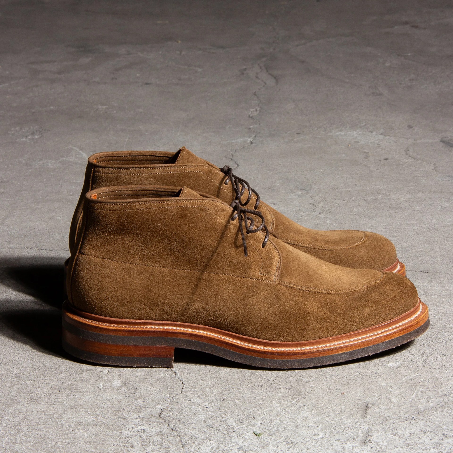 Pair of brown suede leather boots with dark brown laces and wooden soles on concrete floor.