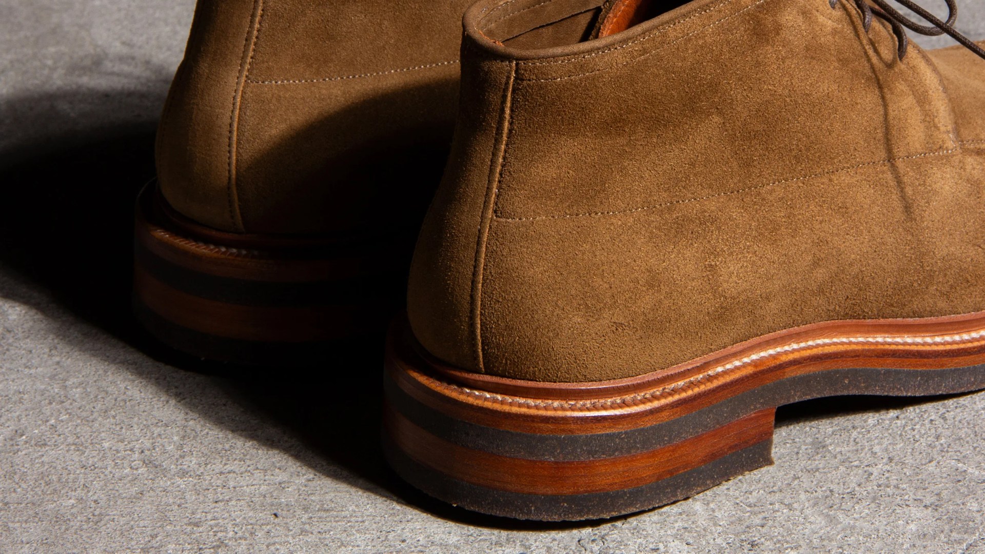 Close-up of brown suede boots with stacked wooden heels on a concrete surface.