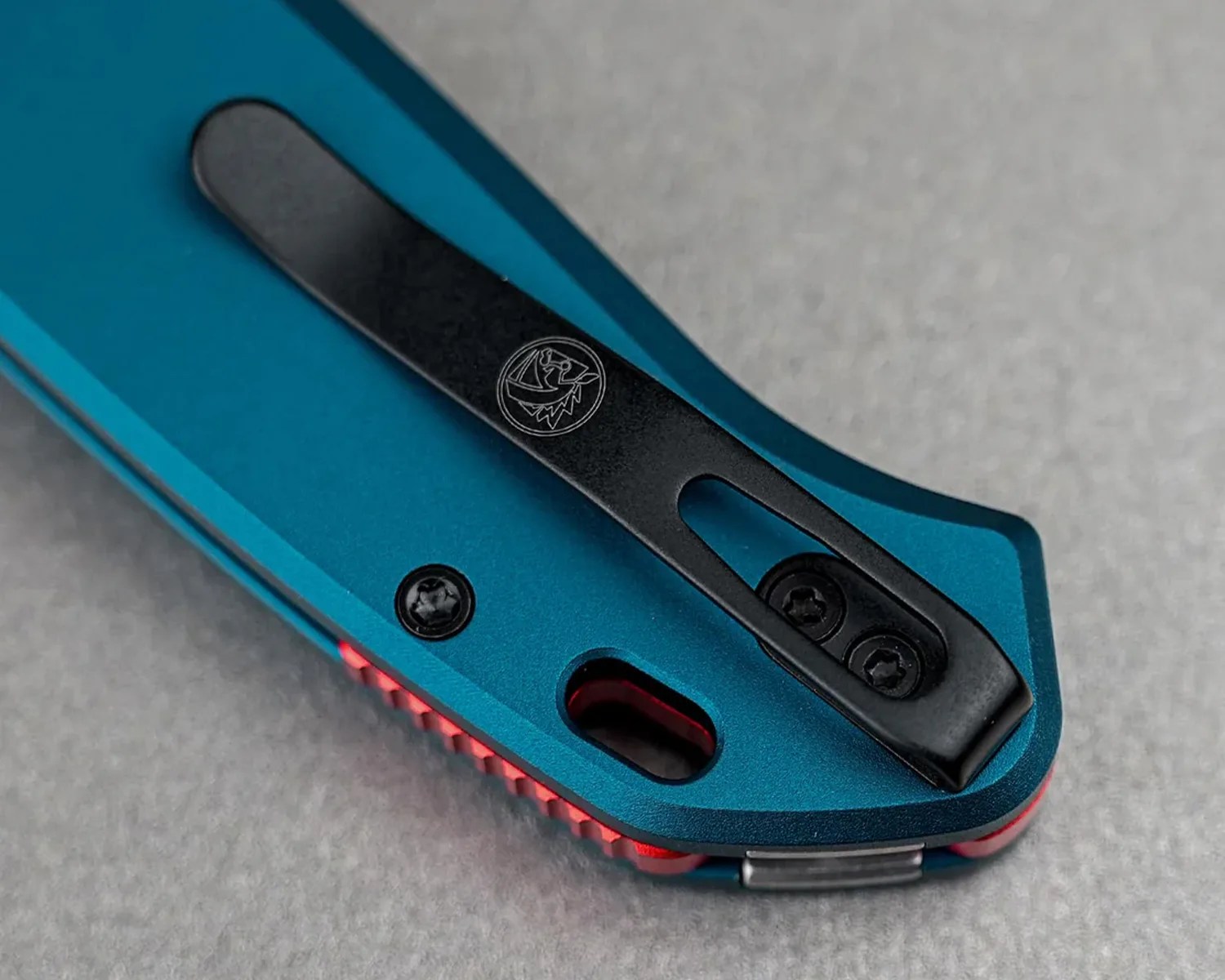 Close-up of a blue folding knife handle with a black pocket clip featuring an engraved logo.