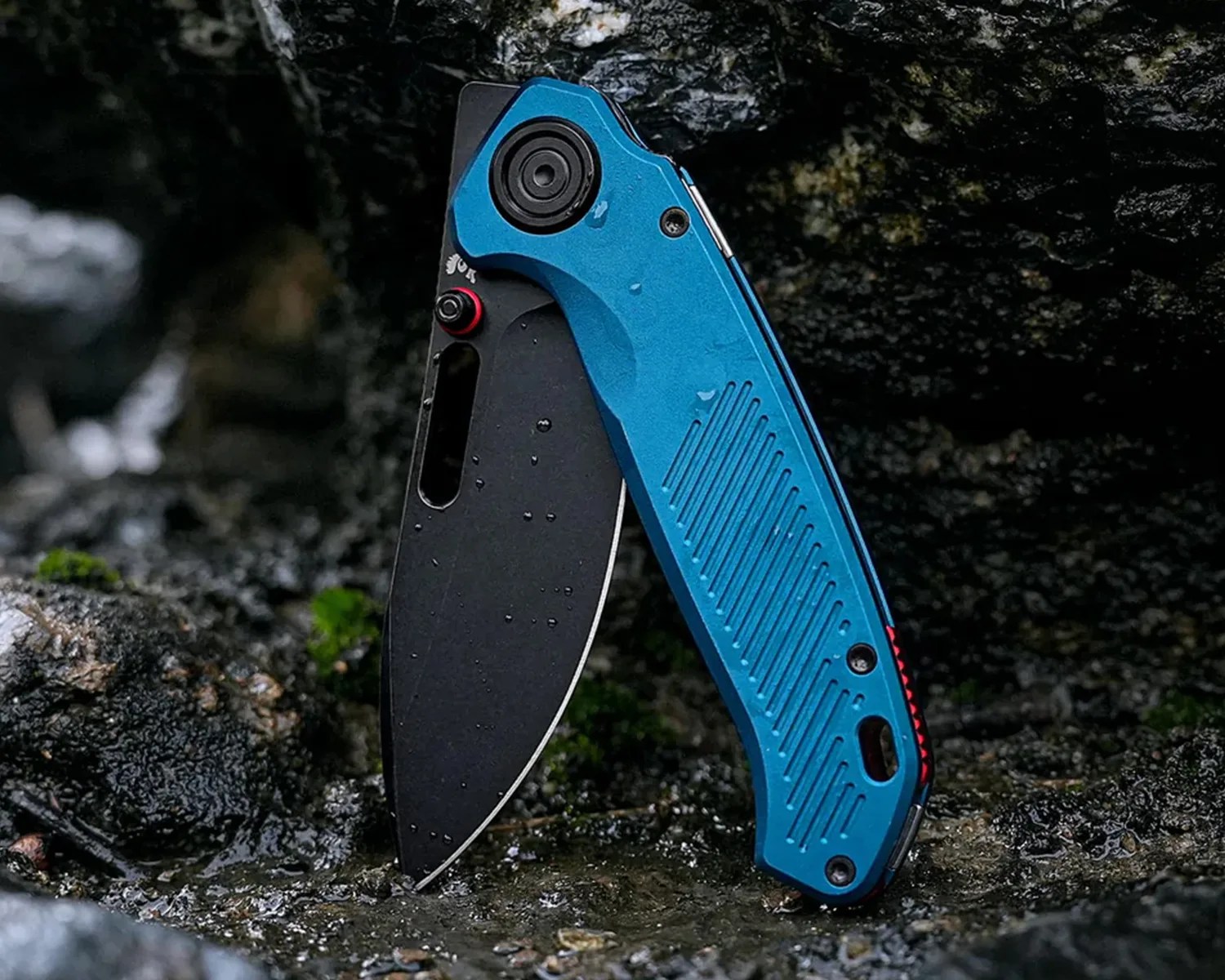 Blue folding knife with a black blade standing open on wet rocky ground.