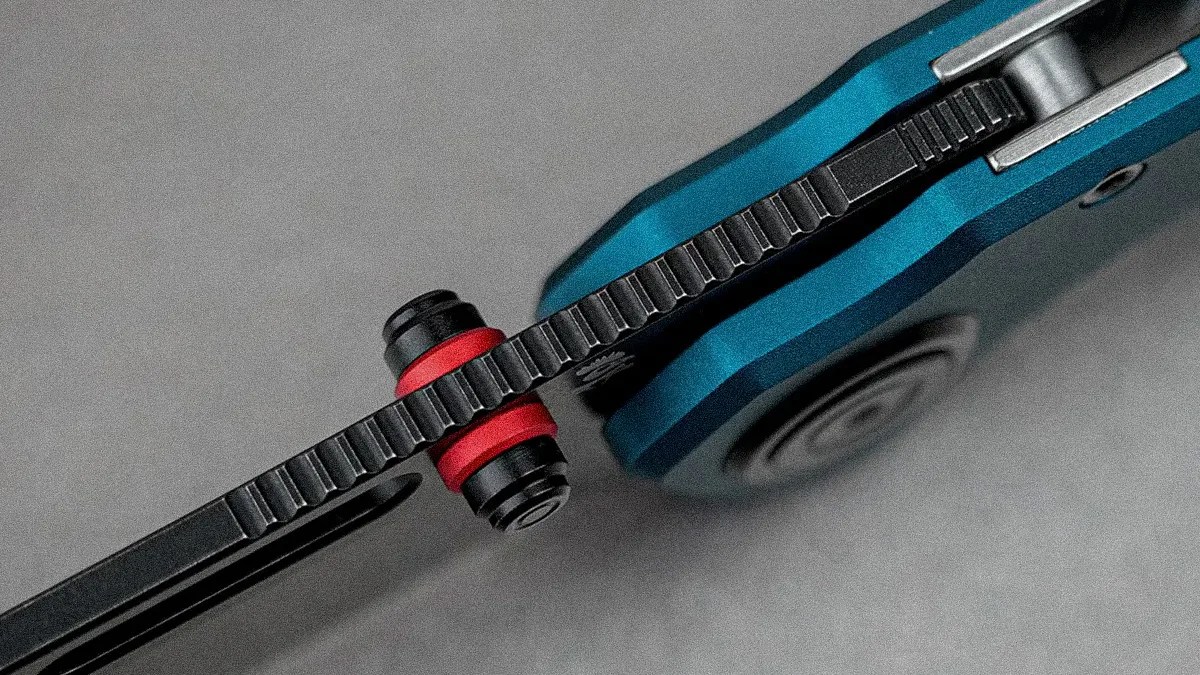 Close-up of a blue folding knife's black textured locking mechanism with red washers on a gray background.