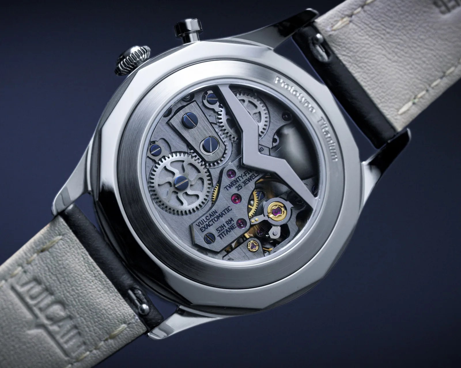 Close-up of a mechanical watch movement with visible gears and screws inside a polished titanium case with a leather strap.