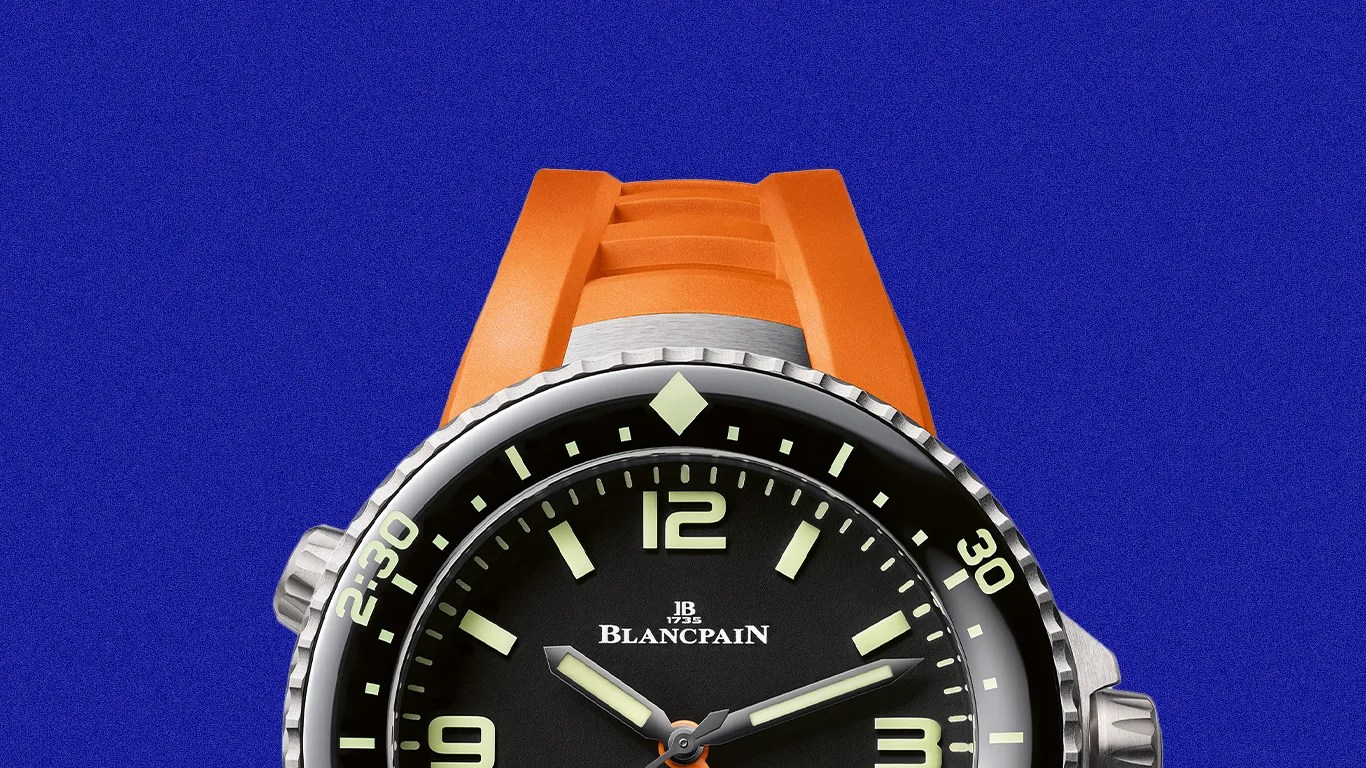 Blancpain dive watch with black dial, luminous markers, and orange rubber strap on blue background.
