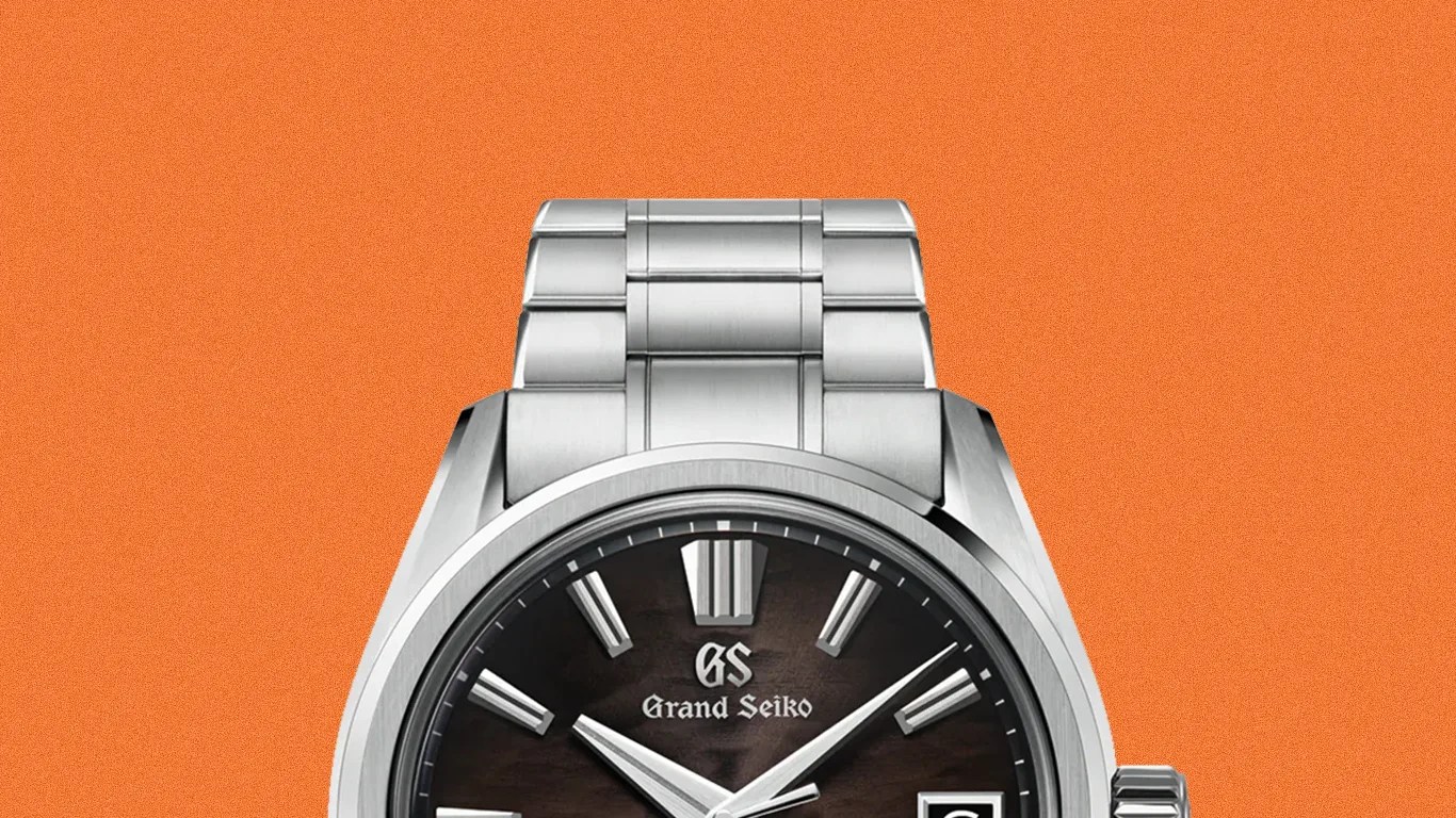Silver Grand Seiko wristwatch with a dark textured dial and metal link bracelet on an orange background.
