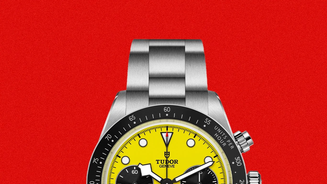Stainless steel Tudor wristwatch with a bright yellow dial, black subdials, and a black tachymeter bezel on a red background.