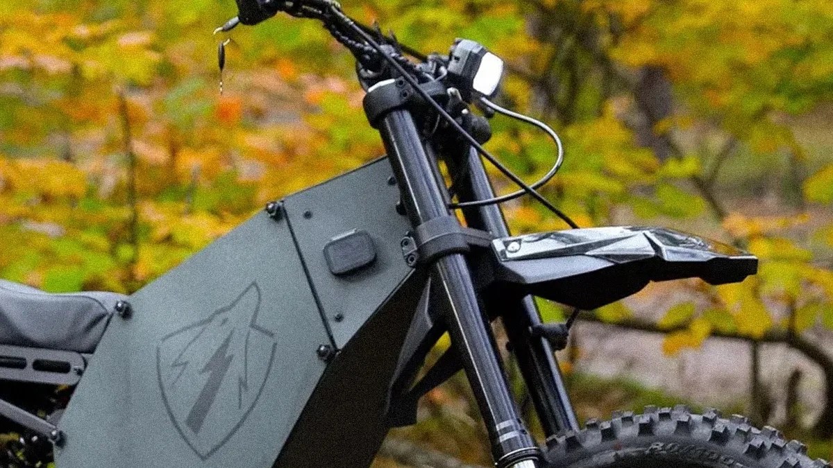 Close-up of the front section of a matte black electric dirt bike with a shield logo and lightning bolt on the side panel.