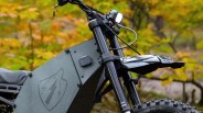 Close-up of the front section of a matte black electric dirt bike with a shield logo and lightning bolt on the side panel.