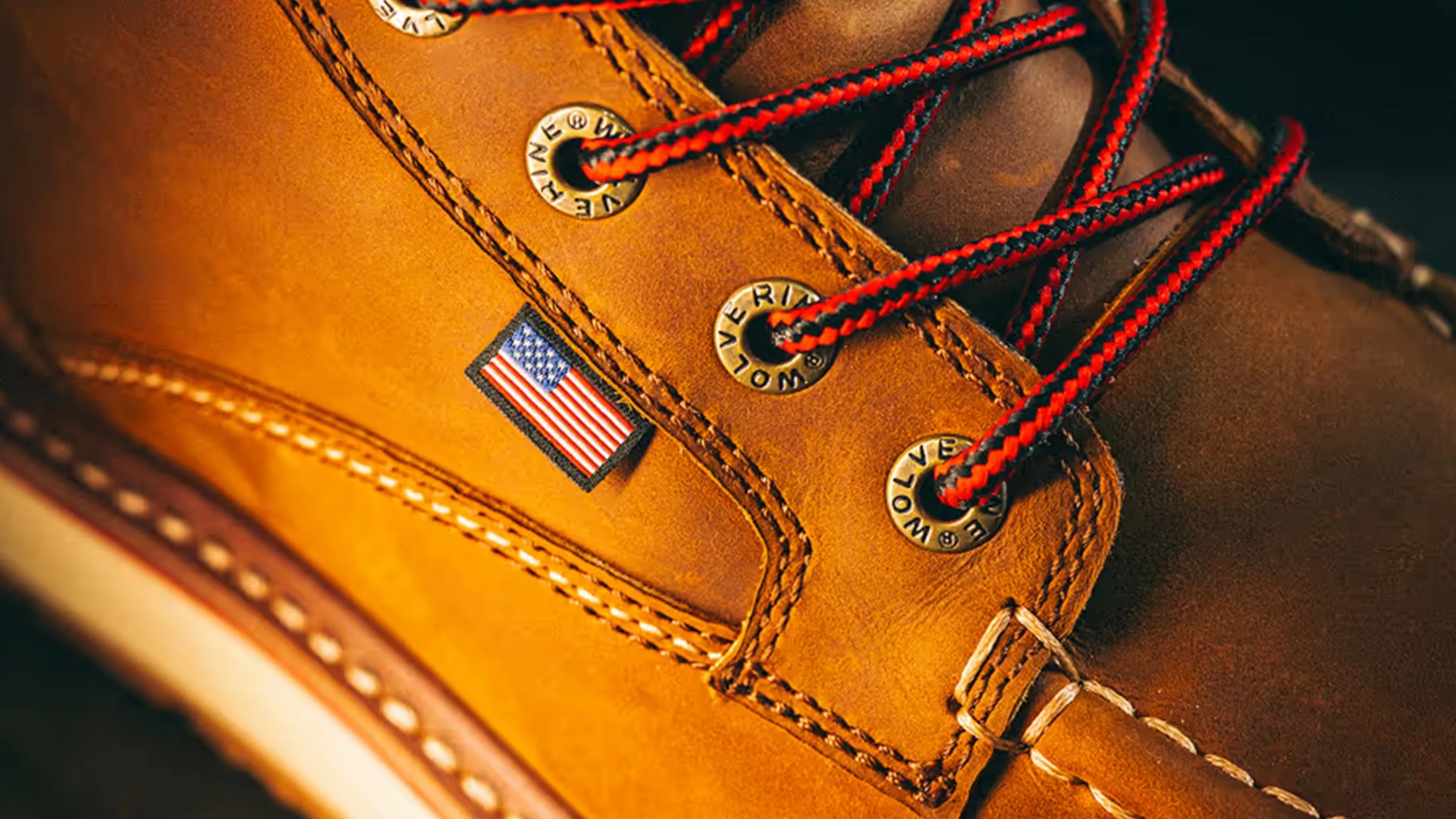 Close-up of a tan leather boot with red and black laces and a small American flag tag.